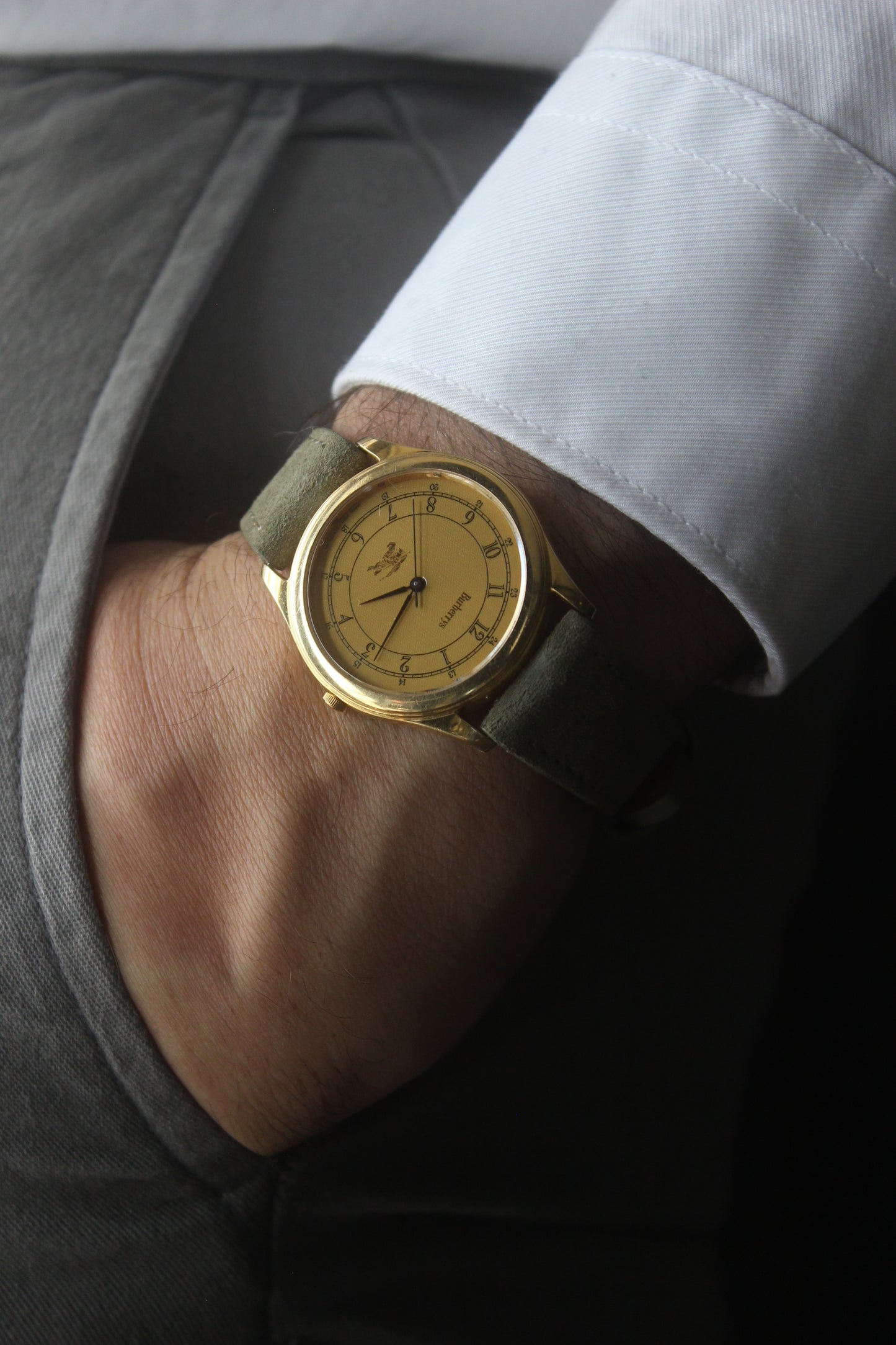 Vintage Burberrys wristwatch with a gold-tone round case, yellow dial featuring black Arabic numerals for both 12-hour and 24-hour markers, and an elegant black logo crest at the 6 o'clock position. The watch is paired with a green suede strap, showcasing a sophisticated and timeless design. Made in Japan, model number 2280-223465 TA, 412018 0.