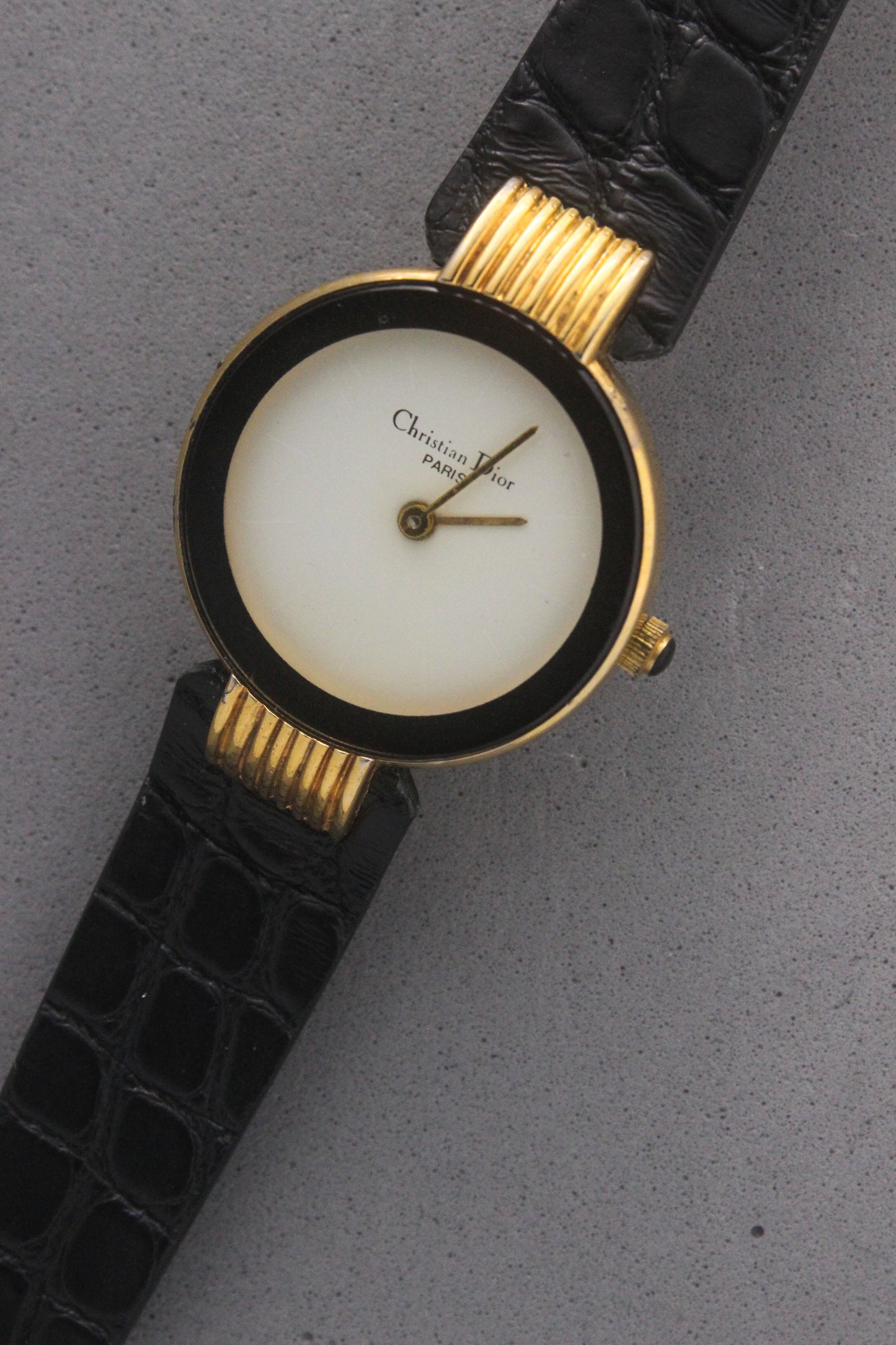 Elegant Christian Dior Paris vintage watch featuring a minimalist gold-plated round case, black enamel bezel, sleek black alligator leather strap, and classic white dial with gold-tone hands. A luxurious and timeless accessory for discerning collectors and fashion enthusiasts. ref. 900-11