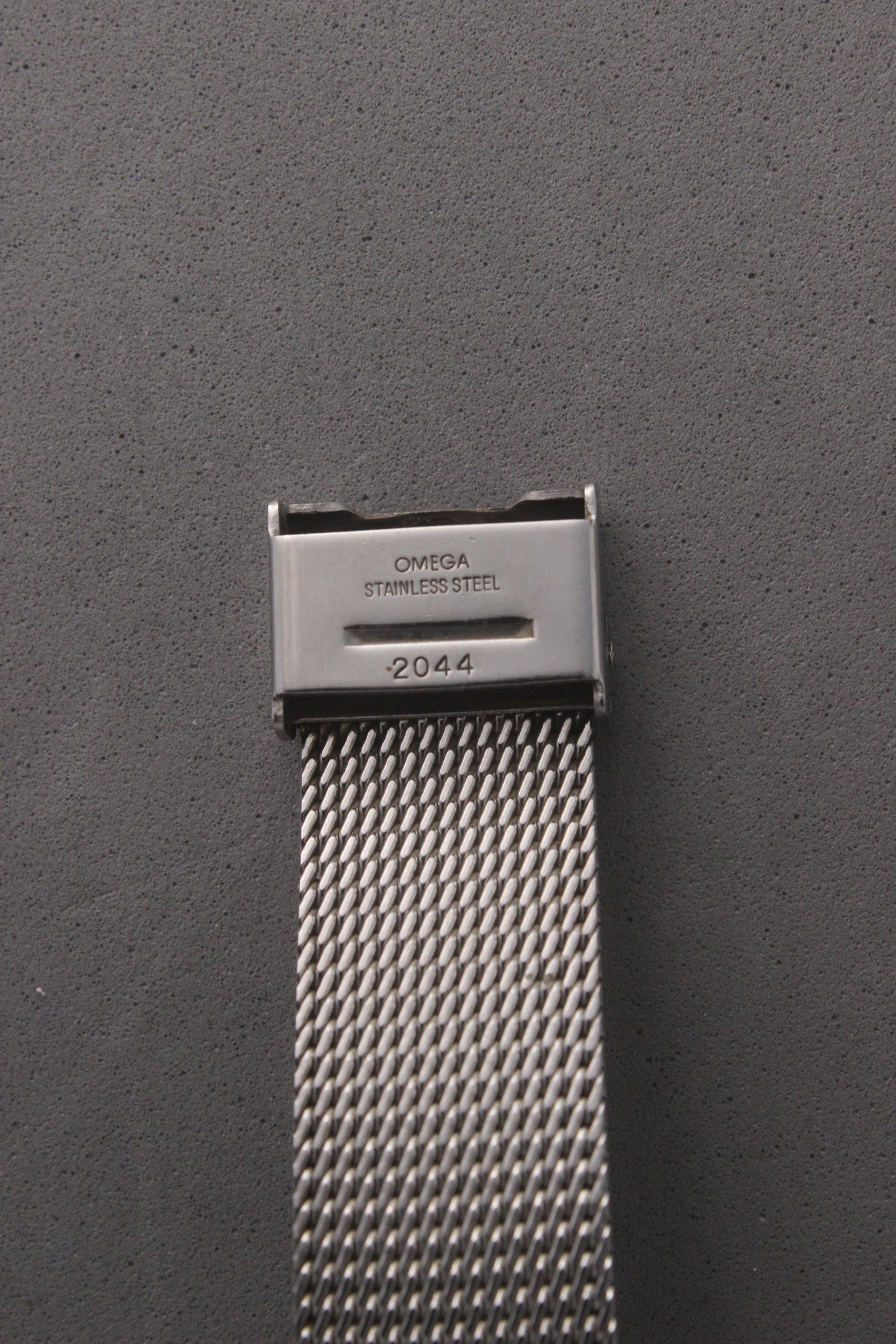 Detailed view of the clasp on the Omega Genève watch, reference number 132.0052, engraved with ‘OMEGA Stainless Steel’ and the serial number ‘2044.’ Highlights the precision craftsmanship and authenticity of the stainless steel mesh bracelet, designed for durability and style.