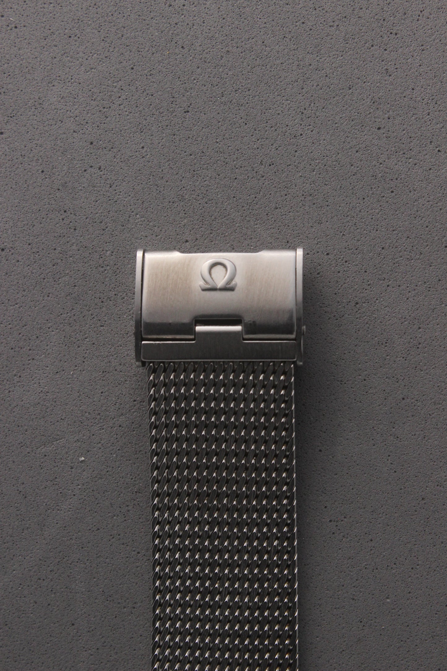 Close-up view of the Omega Genève watch clasp, reference number 132.0052, featuring the iconic Omega logo engraved on the brushed stainless steel surface. Highlights the secure and stylish closure of the mesh bracelet, embodying luxury and timeless elegance.