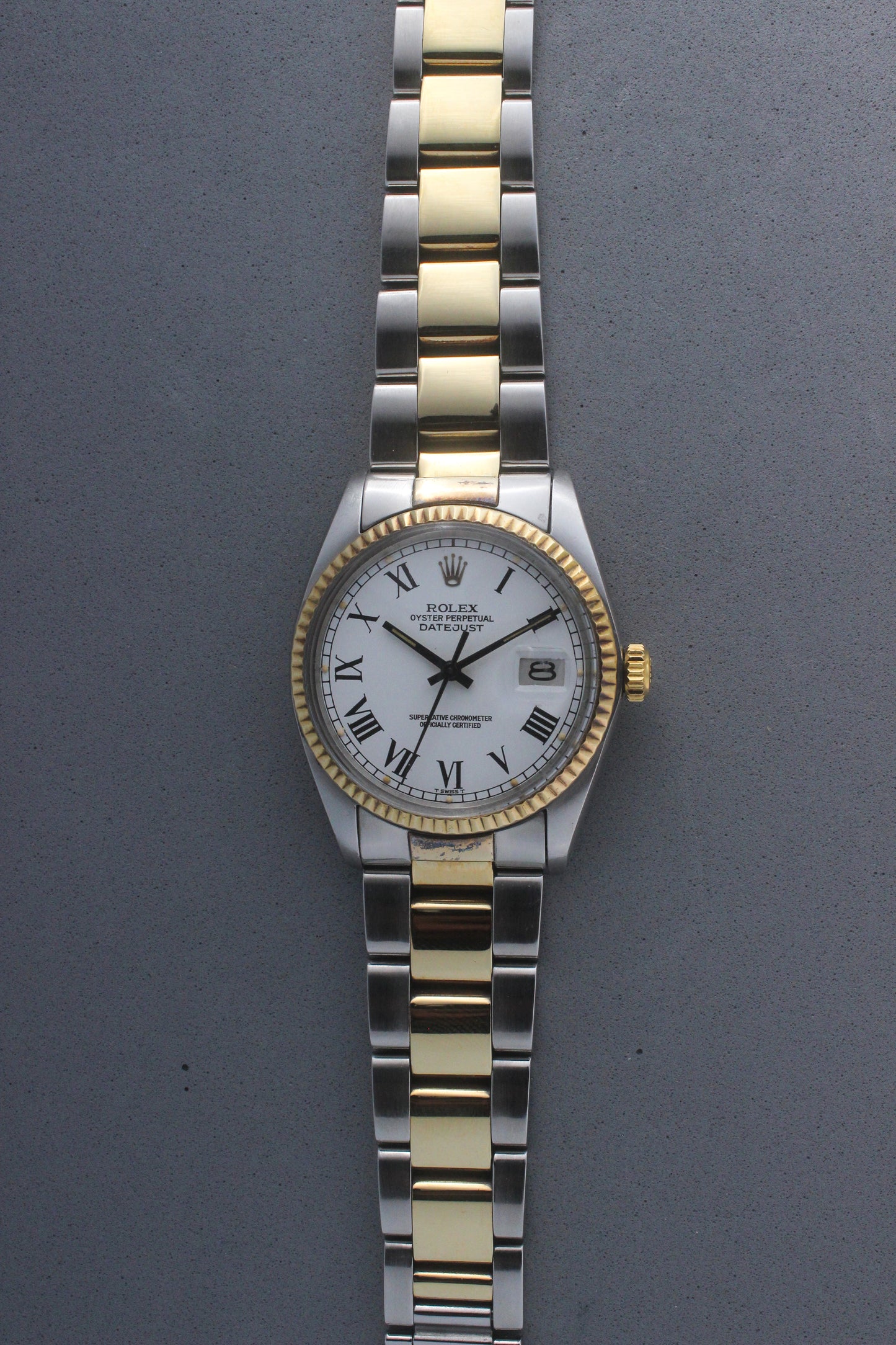 Rolex Datejust reference number 16013, featuring a two-tone stainless steel and yellow gold Jubilee bracelet, a fluted yellow gold bezel, and a classic white dial with black Roman numeral hour markers. The watch includes a date window at 3 o’clock, magnified by a Cyclops lens, and the ‘Rolex Oyster Perpetual Datejust’ text on the dial, showcasing its timeless and elegant design.