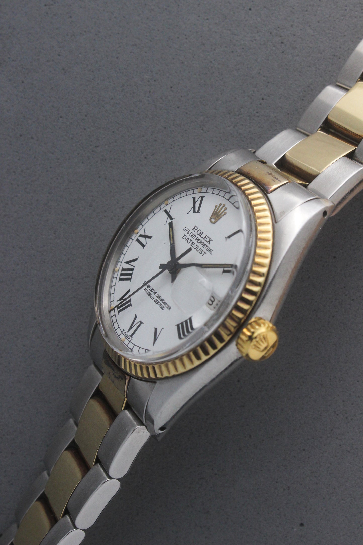 Rolex Datejust reference number 16013, featuring a two-tone stainless steel and yellow gold Jubilee bracelet, a fluted yellow gold bezel, and a classic white dial with black Roman numeral hour markers. The watch includes a date window at 3 o’clock, magnified by a Cyclops lens, and the ‘Rolex Oyster Perpetual Datejust’ text on the dial, showcasing its timeless and elegant design.
