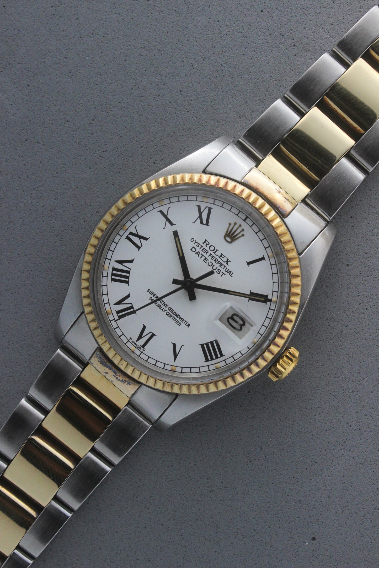 Rolex Datejust reference number 16013, featuring a two-tone stainless steel and yellow gold Jubilee bracelet, a fluted yellow gold bezel, and a classic white dial with black Roman numeral hour markers. The watch includes a date window at 3 o’clock, magnified by a Cyclops lens, and the ‘Rolex Oyster Perpetual Datejust’ text on the dial, showcasing its timeless and elegant design.