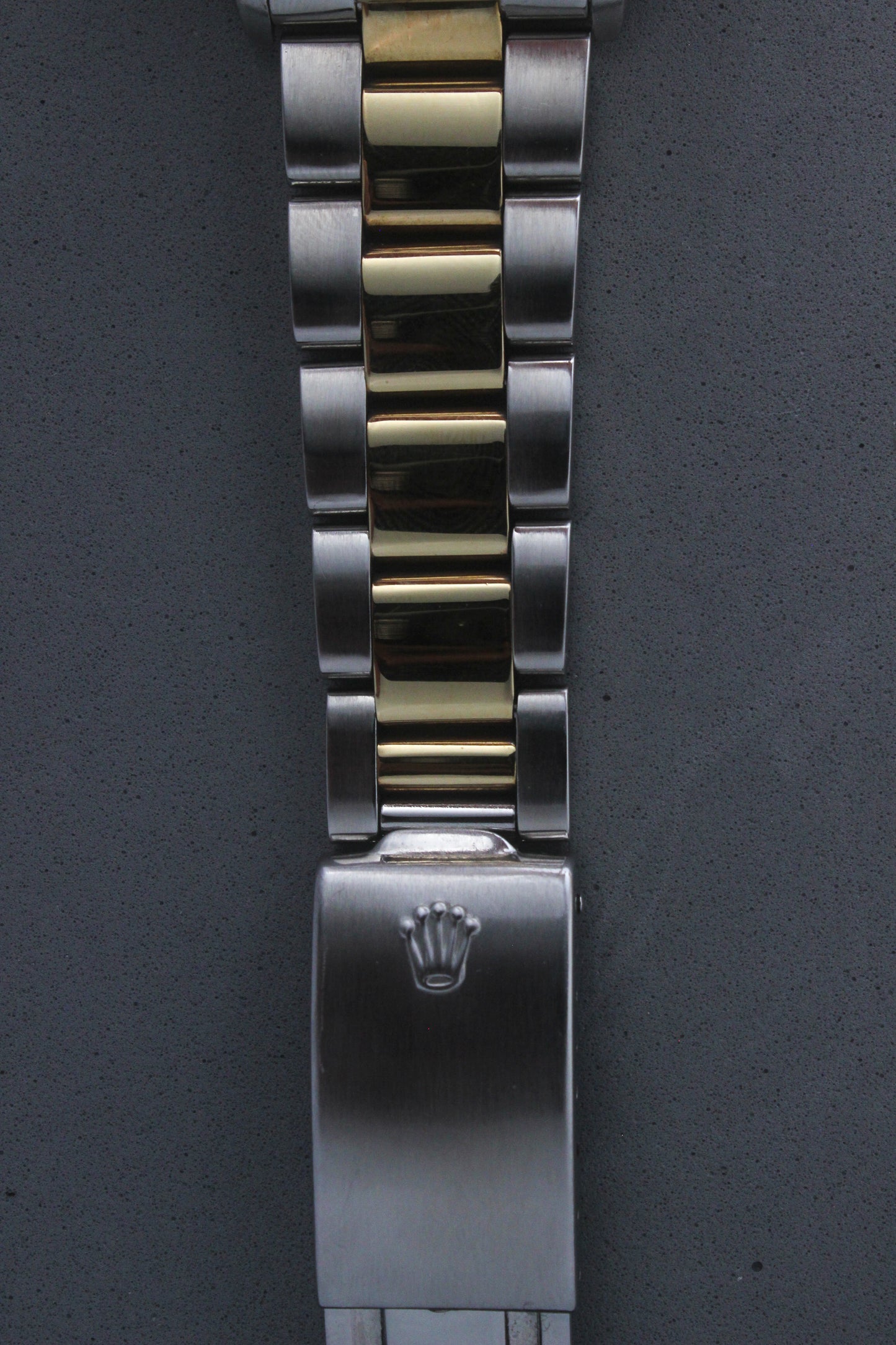 Detailed view of the Rolex Datejust reference number 16013 bracelet clasp, featuring the iconic Rolex coronet embossed on the brushed stainless steel clasp. The image also highlights the two-tone Jubilee bracelet, combining polished yellow gold center links and brushed stainless steel outer links, reflecting the brand’s luxury aesthetic.