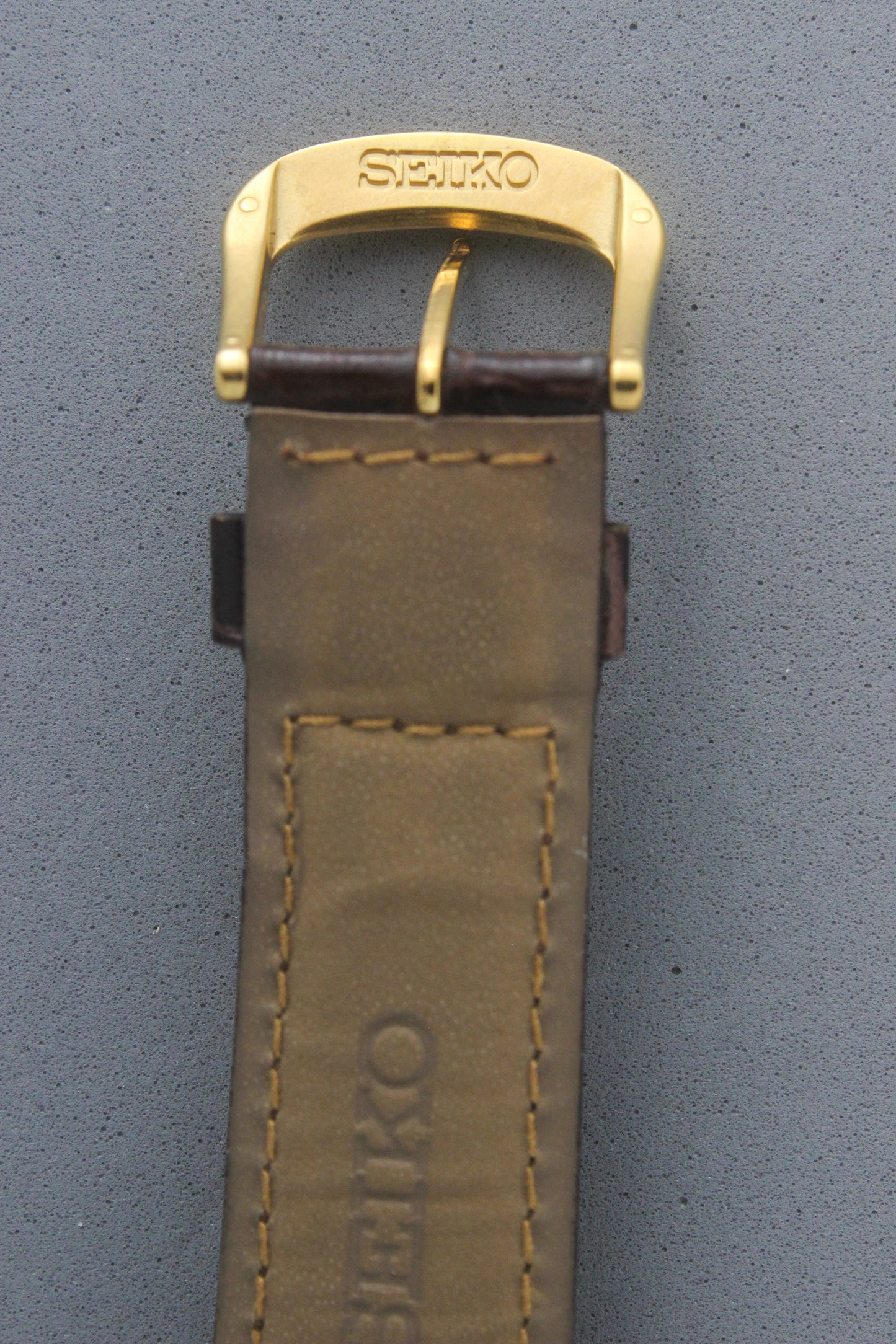 Close-up of the Seiko gold-tone buckle, engraved with the "Seiko" logo, attached to the brown leather strap. The secure fastening system adds functionality to the luxurious aesthetic of the 8F32-0140 model.
