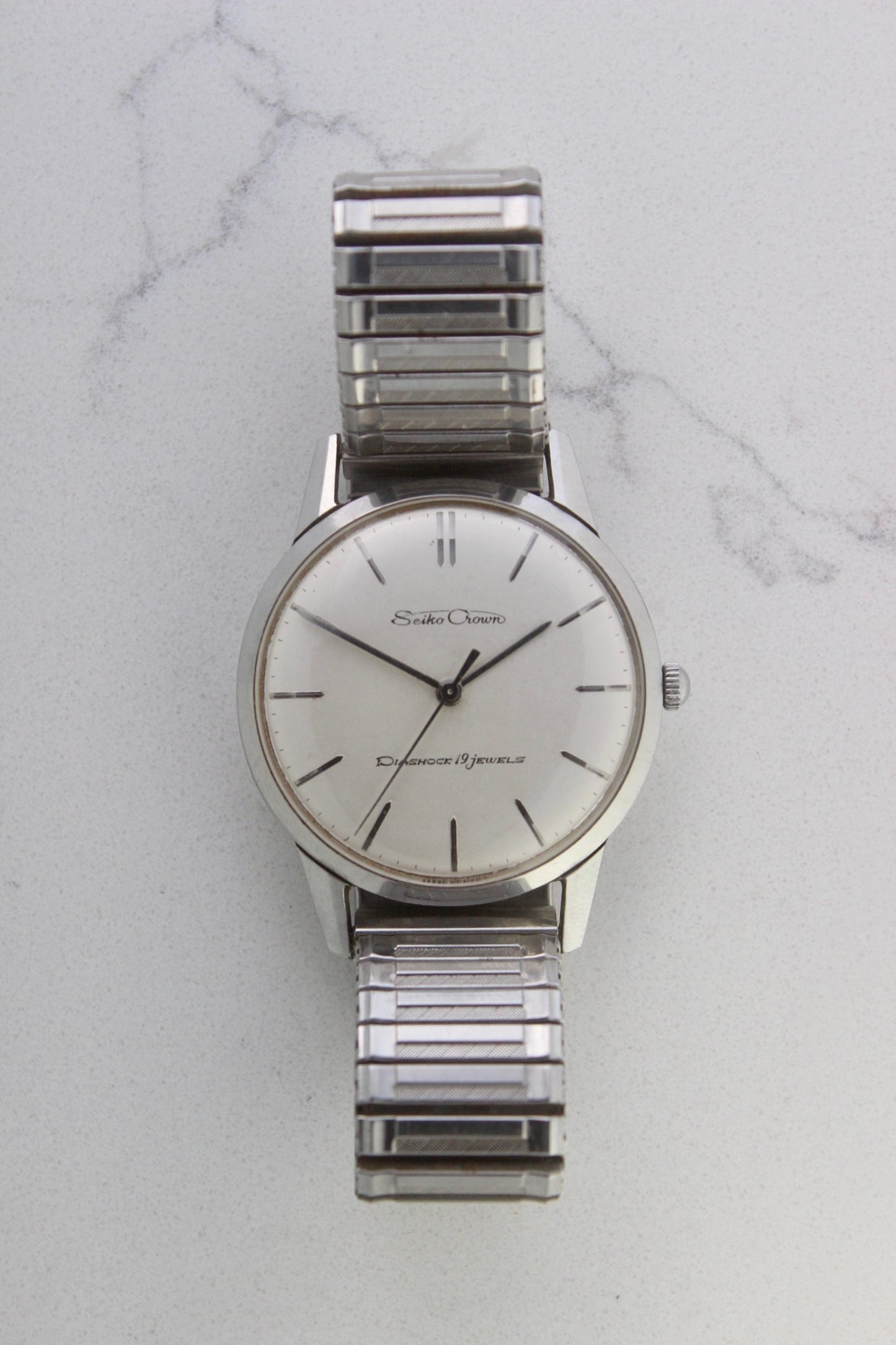 Vintage Seiko Crown 35.5mm stainless steel manual-wind watch from July 1960. Features a flat satin silver lacquered dial with silver indices, a double logo at the 12 and 6 o’clock positions, and slim silver stick hands for hours, minutes, and seconds. The ultra-slim 10mm case is complemented by a stainless steel fixed bezel and a vintage-style stretch bracelet with brushed and polished surfaces. In great condition with minimal signs of wear on the bracelet and crystal. A rare collector's piece.