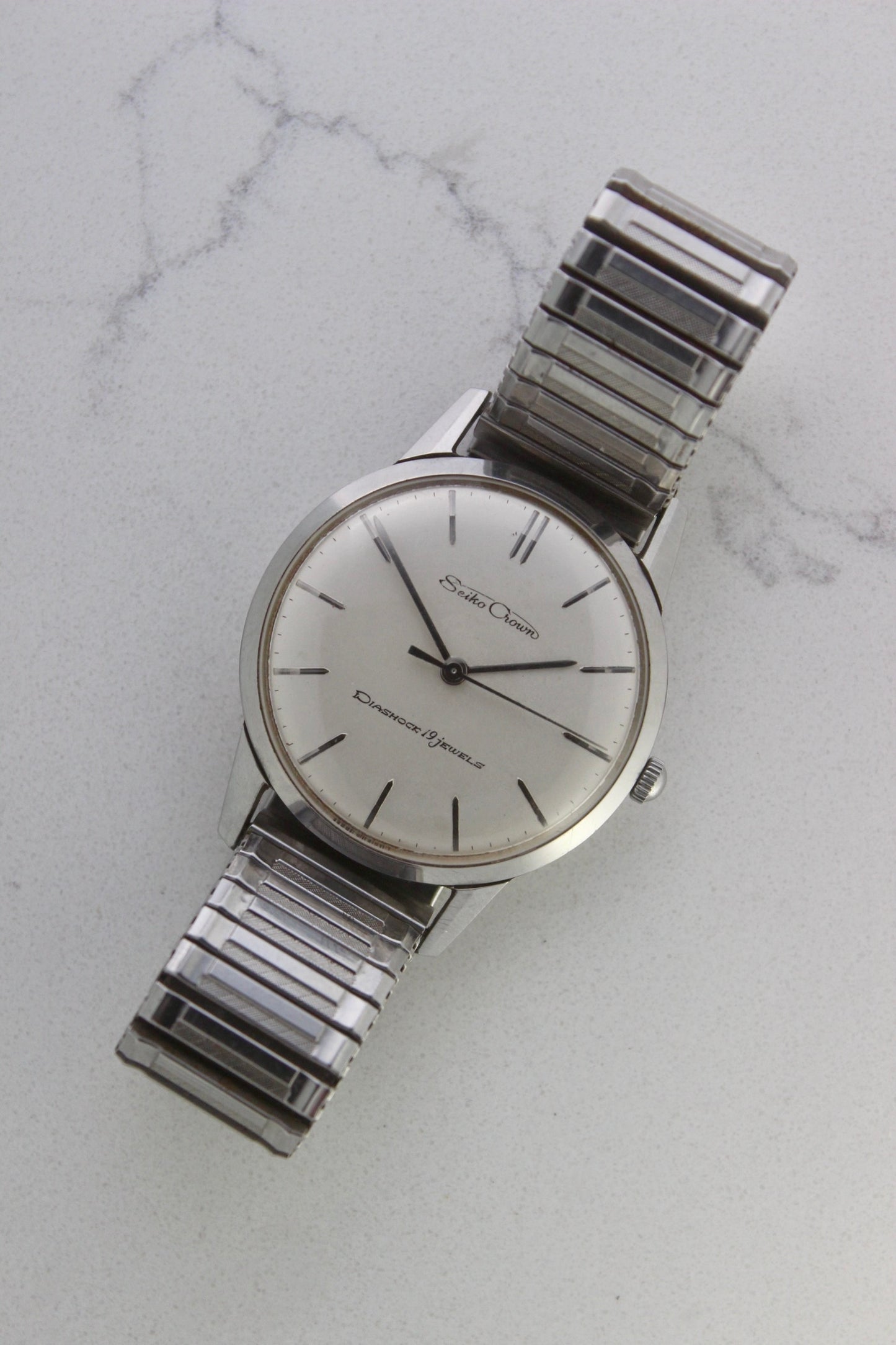 Vintage Seiko Crown 35.5mm stainless steel manual-wind watch from July 1960. Features a flat satin silver lacquered dial with silver indices, a double logo at the 12 and 6 o’clock positions, and slim silver stick hands for hours, minutes, and seconds. The ultra-slim 10mm case is complemented by a stainless steel fixed bezel and a vintage-style stretch bracelet with brushed and polished surfaces. In great condition with minimal signs of wear on the bracelet and crystal. A rare collector's piece.