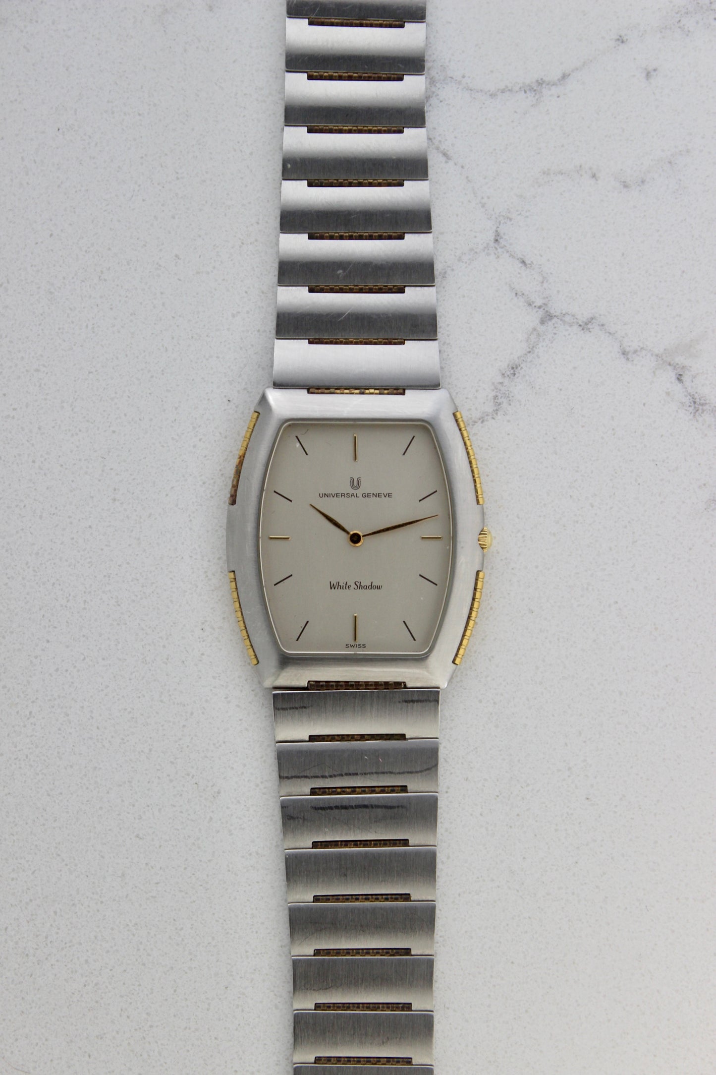 Front View of Universal Genève White Shadow Ref. 617-020
A close-up of the Universal Genève White Shadow Ref. 617-020, featuring a sleek tonneau-shaped stainless steel case with gold accents, a clean white dial, and minimalist stick hands and indices. Paired with an integrated stainless steel bracelet for timeless elegance.