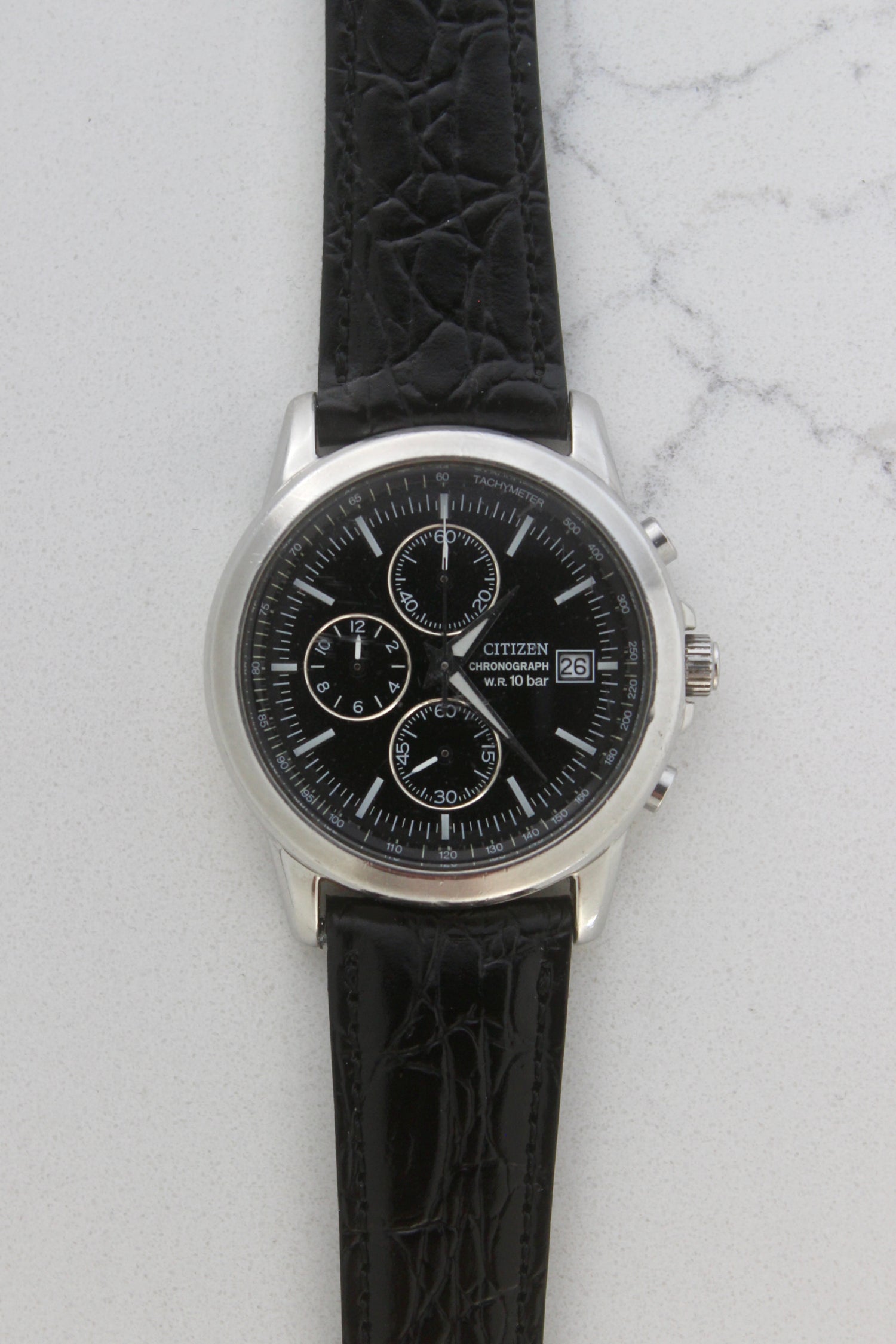 Citizen Chronograph Watch with black dial and black leather strap, featuring a tachymeter scale, water resistance up to 10 bar, and reference number 0510-K002320.