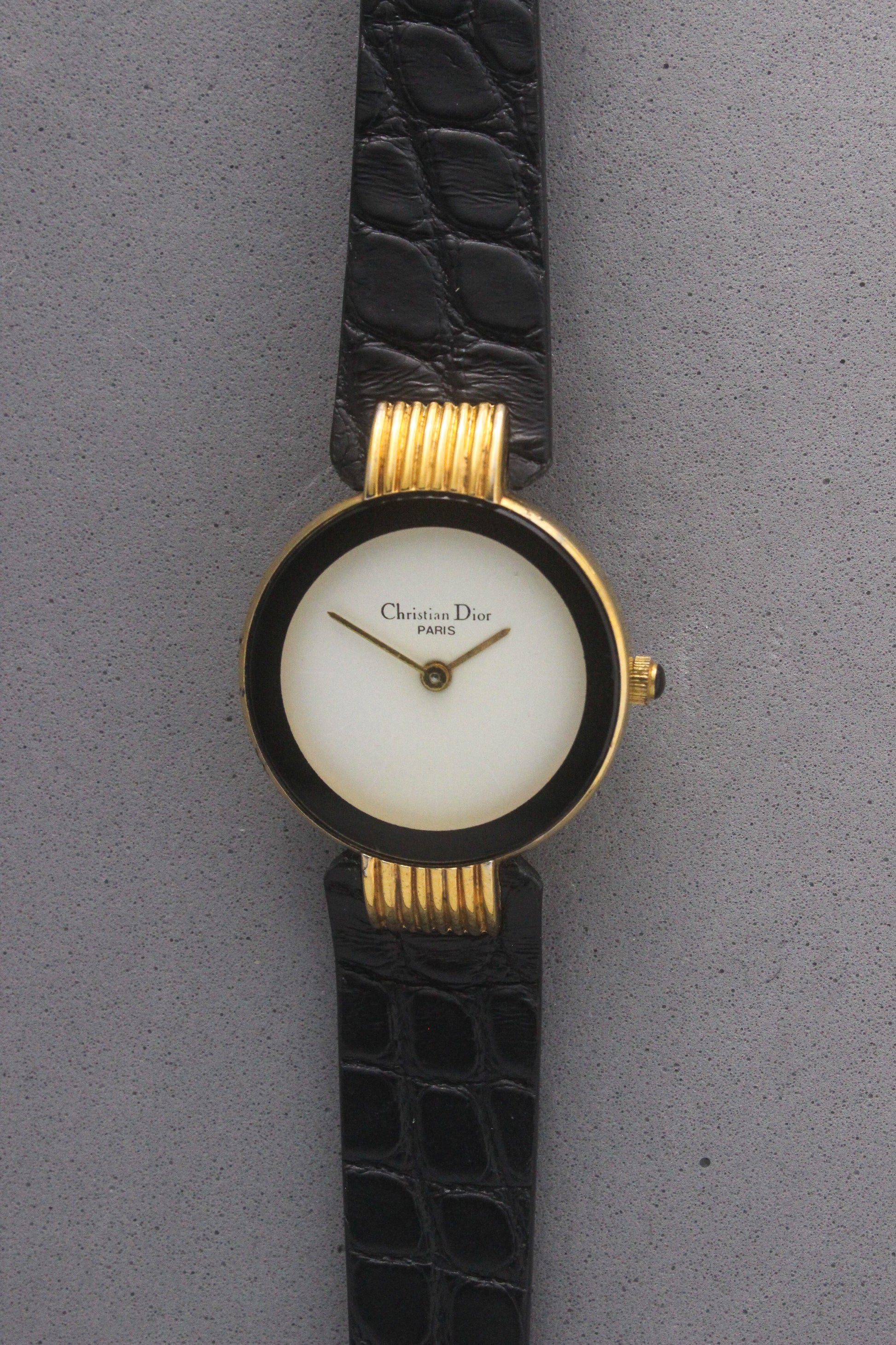 Elegant Christian Dior Paris vintage watch featuring a minimalist gold-plated round case, black enamel bezel, sleek black alligator leather strap, and classic white dial with gold-tone hands. A luxurious and timeless accessory for discerning collectors and fashion enthusiasts.ref. 900-11