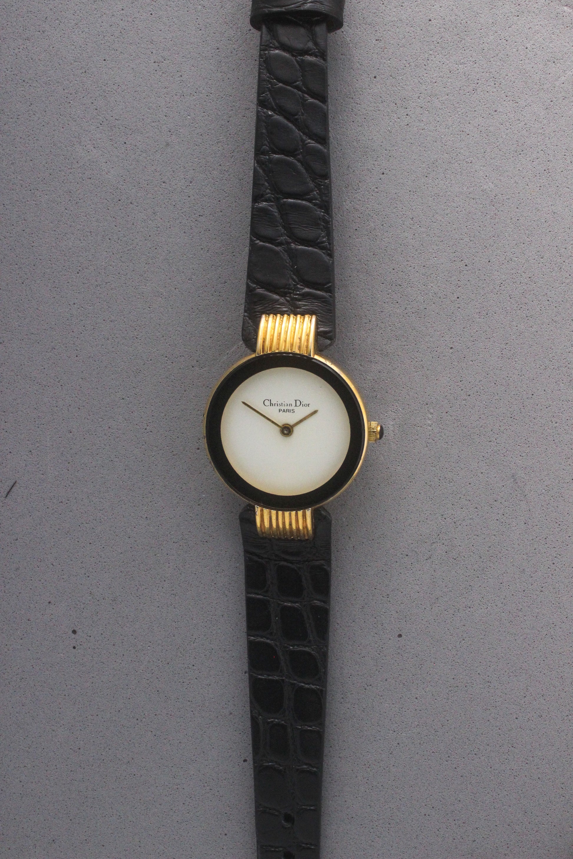 Elegant Christian Dior Paris vintage watch featuring a minimalist gold-plated round case, black enamel bezel, sleek black alligator leather strap, and classic white dial with gold-tone hands. A luxurious and timeless accessory for discerning collectors and fashion enthusiasts. ref. 900-11
