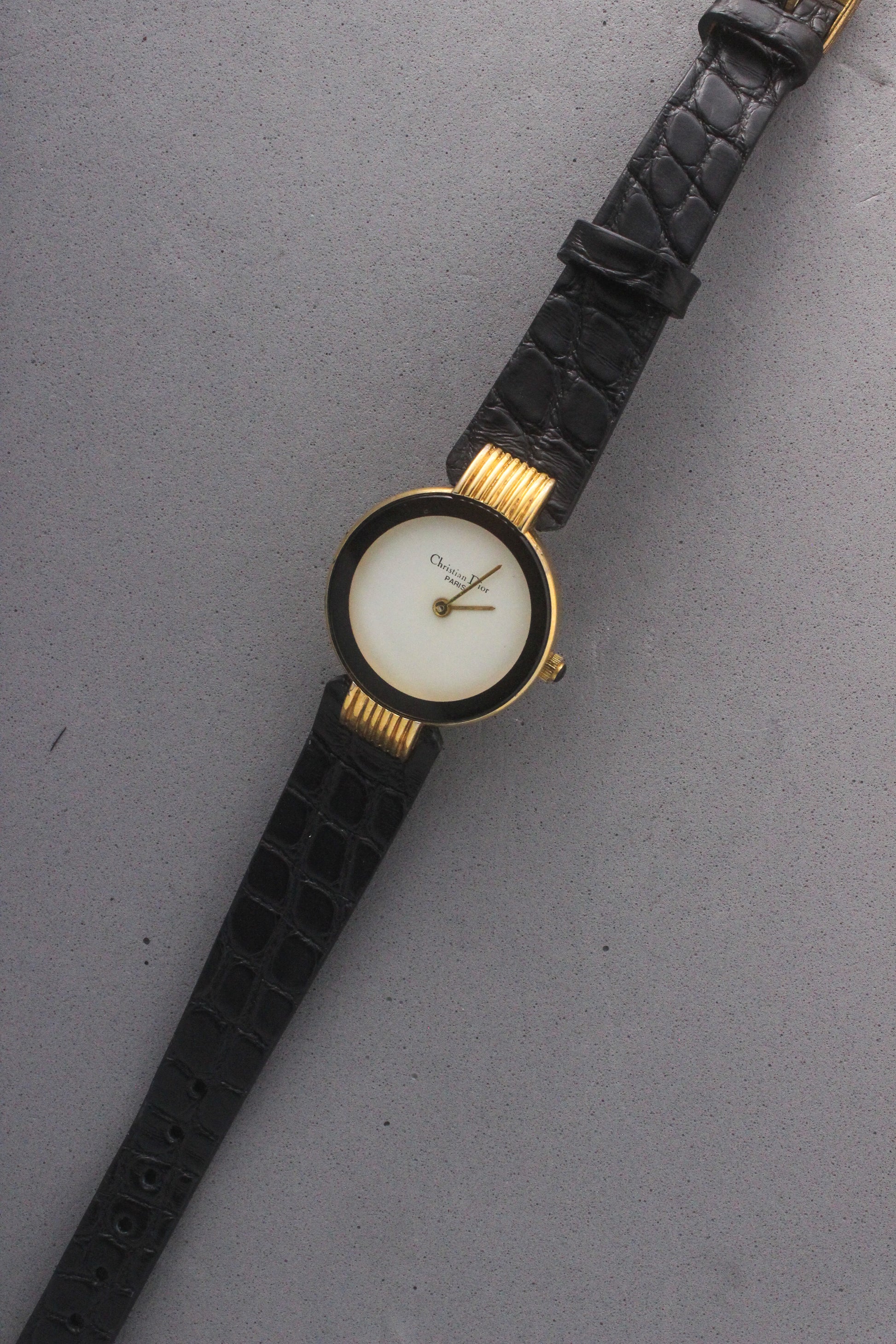 Elegant Christian Dior Paris vintage watch featuring a minimalist gold-plated round case, black enamel bezel, sleek black alligator leather strap, and classic white dial with gold-tone hands. A luxurious and timeless accessory for discerning collectors and fashion enthusiasts. ref. 900-11