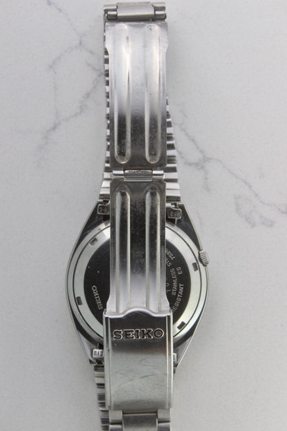 The stainless steel bracelet and clasp of a vintage Seiko 5 automatic wristwatch (Reference Number: 7S26-3040). The fold-over clasp is engraved with the Seiko logo and shows visible surface scratches, indicating signs of wear. The original stainless steel bracelet remains intact, with end links marked "B13" and "75-E". This Japan-exclusive mid-1980s model is in good condition with expected wear for its age.