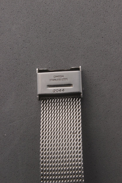 Detailed view of the clasp on the Omega Genève watch, reference number 132.0052, engraved with ‘OMEGA Stainless Steel’ and the serial number ‘2044.’ Highlights the precision craftsmanship and authenticity of the stainless steel mesh bracelet, designed for durability and style.
