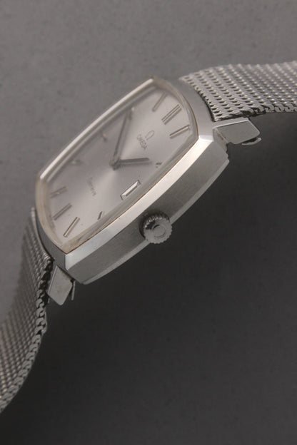 Vintage Omega Genève men’s wristwatch, reference number 132.0052, featuring a sleek silver square case, minimalist silver-tone dial, date display at 3 o’clock, and an elegant stainless steel mesh bracelet. A timeless Swiss-made classic, perfect for collectors and enthusiasts of luxury timepieces.
