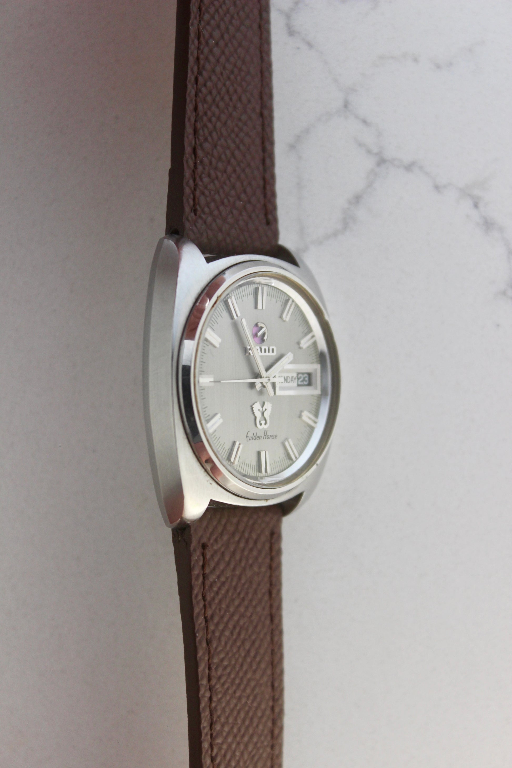 Vintage Rado Golden Horse watch, reference number 11816, featuring brown strap, silver-tone dial with baton hour markers, day-date display at 3 o’clock, and the signature Golden Horse logo. A timeless and elegant collector’s timepiece from Rado.