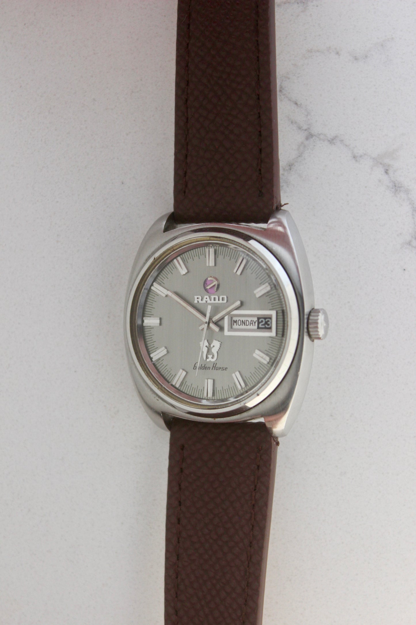 Vintage Rado Golden Horse watch, reference number 11816, featuring brown strap, silver-tone dial with baton hour markers, day-date display at 3 o’clock, and the signature Golden Horse logo. A timeless and elegant collector’s timepiece from Rado.