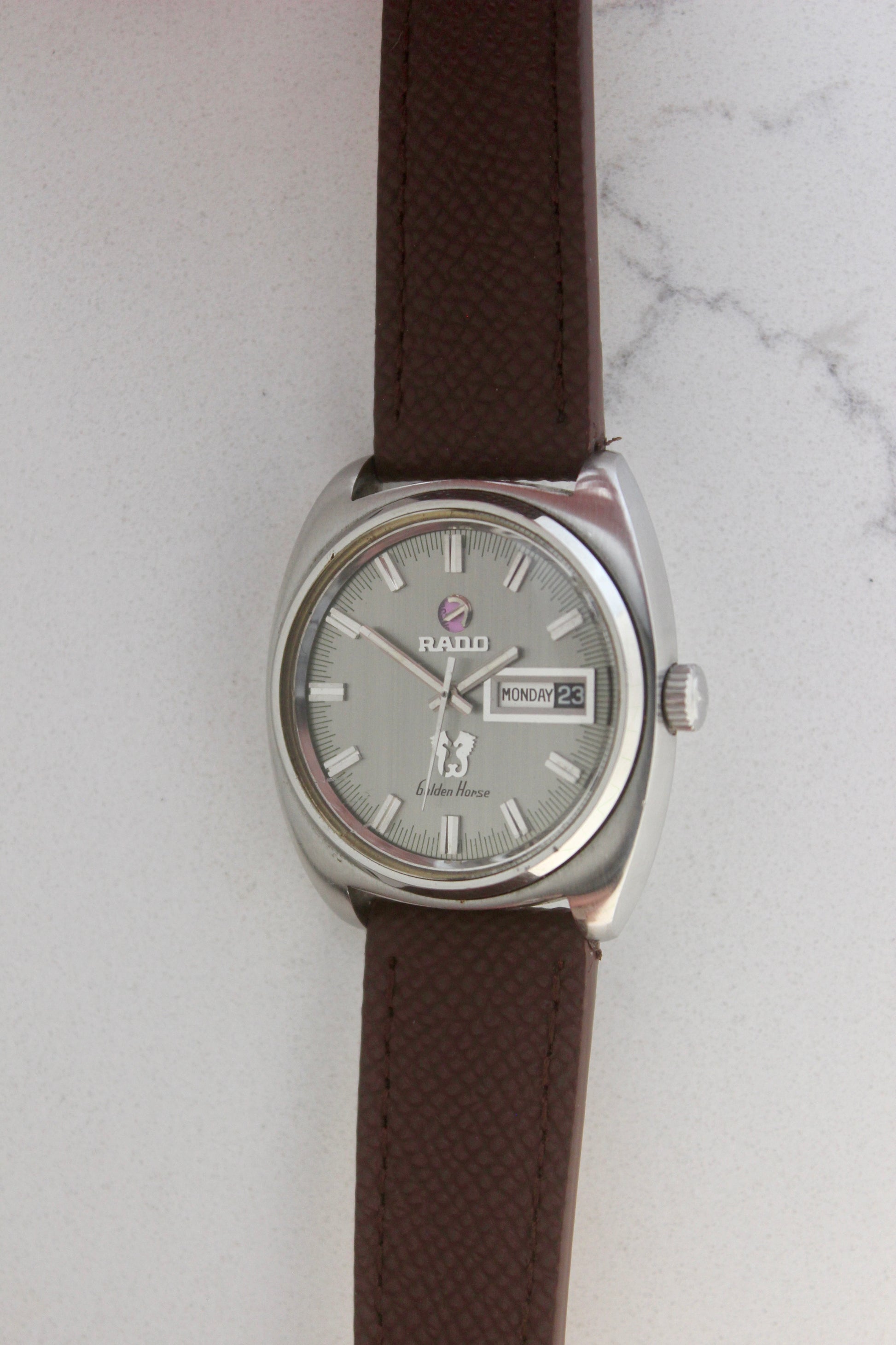 Vintage Rado Golden Horse watch, reference number 11816, featuring brown strap, silver-tone dial with baton hour markers, day-date display at 3 o’clock, and the signature Golden Horse logo. A timeless and elegant collector’s timepiece from Rado.