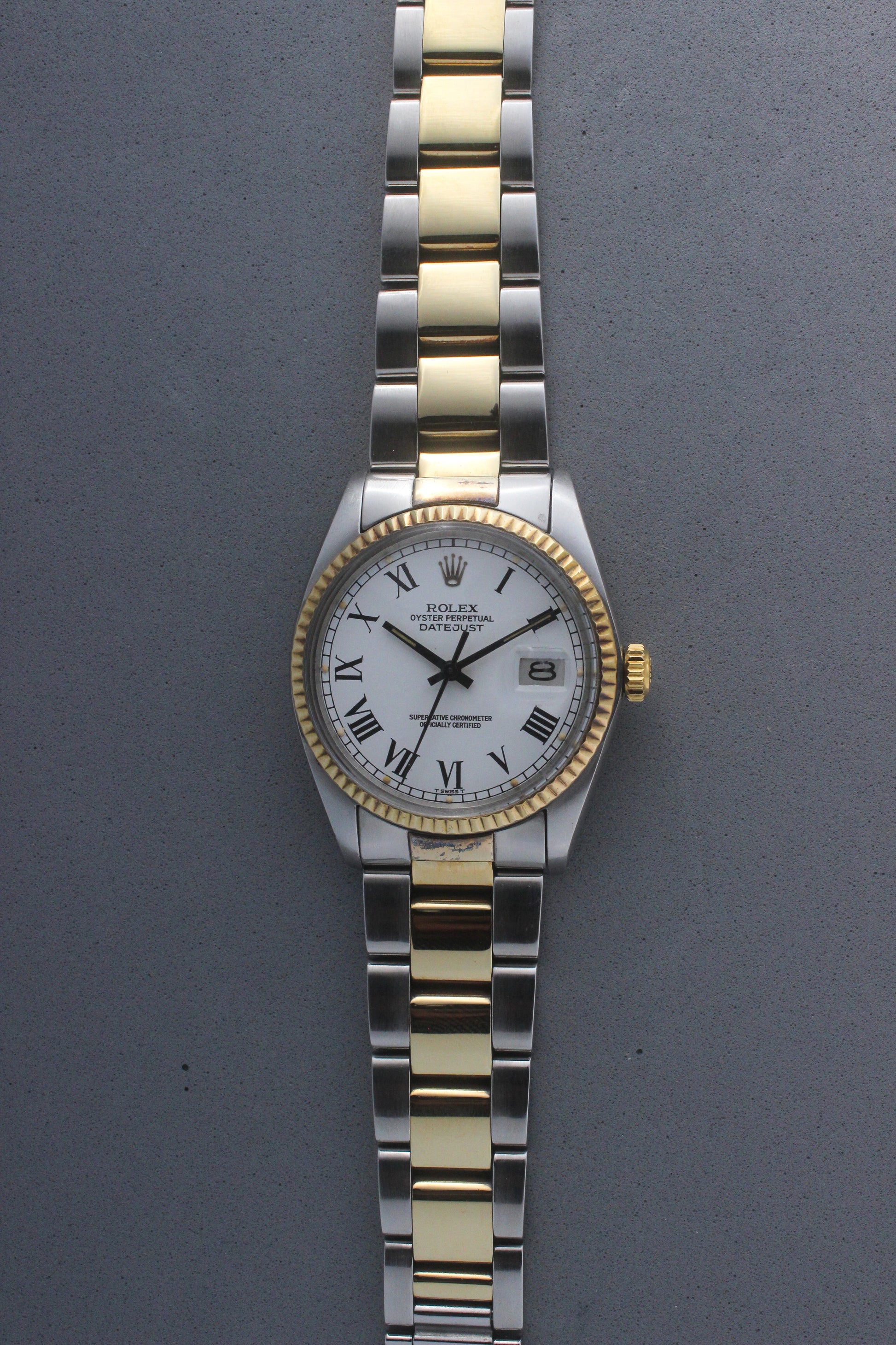 Rolex Datejust reference number 16013, featuring a two-tone stainless steel and yellow gold Jubilee bracelet, a fluted yellow gold bezel, and a classic white dial with black Roman numeral hour markers. The watch includes a date window at 3 o’clock, magnified by a Cyclops lens, and the ‘Rolex Oyster Perpetual Datejust’ text on the dial, showcasing its timeless and elegant design.