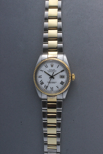 Rolex Datejust reference number 16013, featuring a two-tone stainless steel and yellow gold Jubilee bracelet, a fluted yellow gold bezel, and a classic white dial with black Roman numeral hour markers. The watch includes a date window at 3 o’clock, magnified by a Cyclops lens, and the ‘Rolex Oyster Perpetual Datejust’ text on the dial, showcasing its timeless and elegant design.