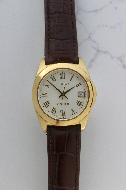 A detailed front view of the Seiko Caster
8F32-0140 watch featuring a gold-tone case, Roman numeral markers, and a date window at 3 o'clock. The cream-colored dial is complemented by classic black hands, encapsulating an elegant vintage aesthetic.
Paired with a genuine brown leather strap.