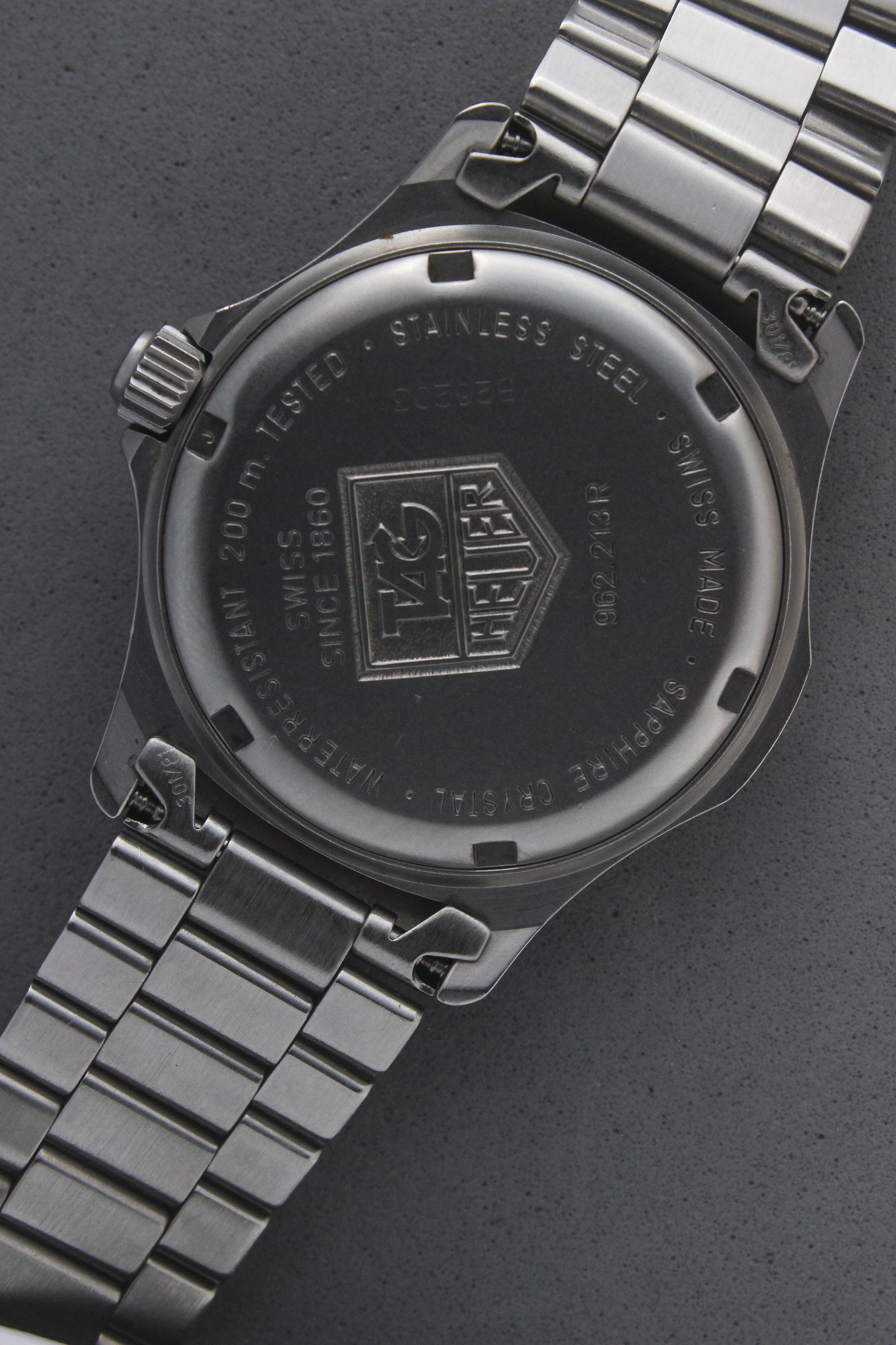 Close-up of the TAG Heuer Professional Ref.
962.213R case back showcasing engravings including "962.213R," "Water Resistant 200m
Tested," and "Swiss Made." The TAG Heuer logo and brushed stainless steel highlight the quality craftsmanship.