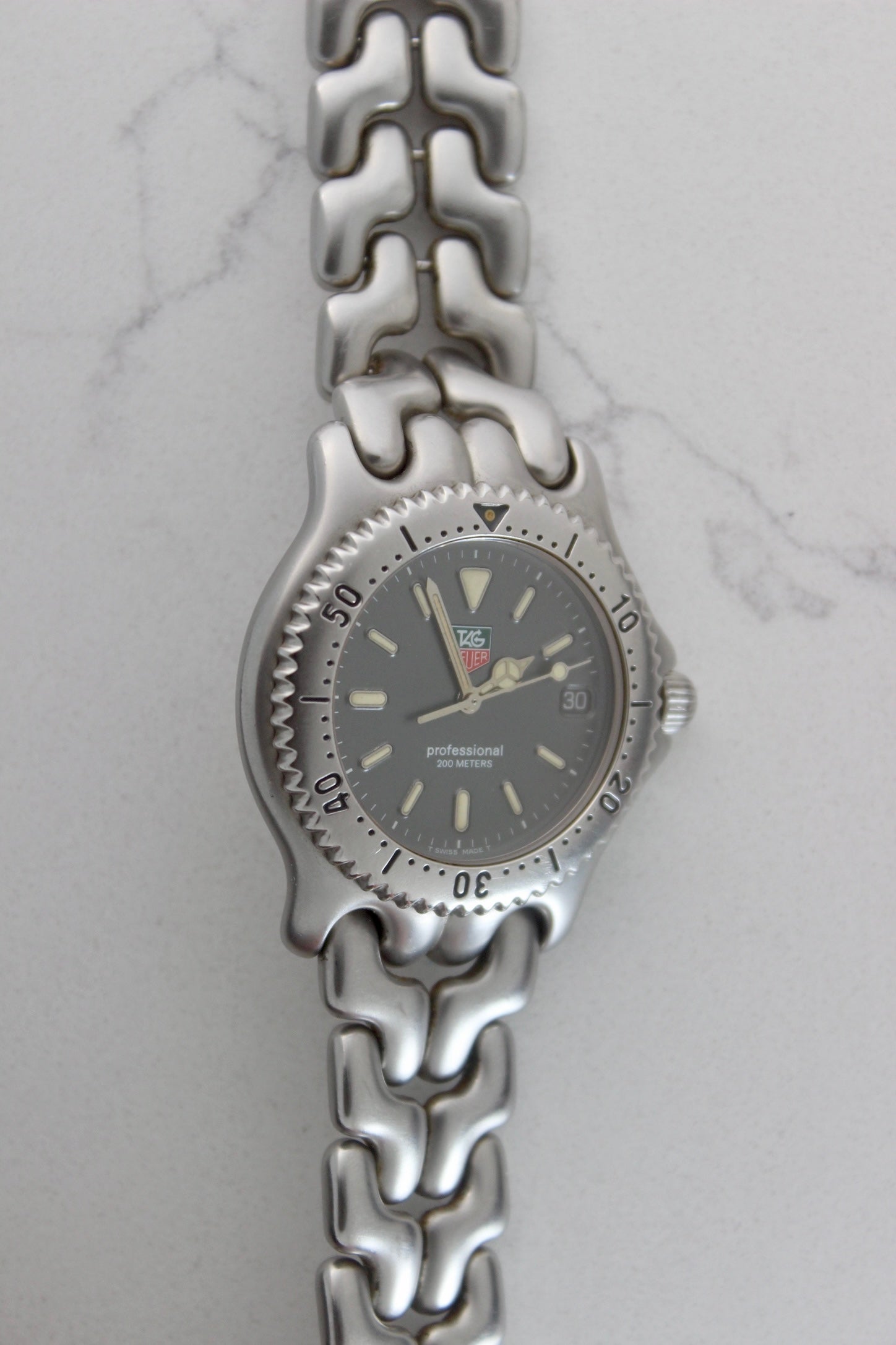 Tag Heuer Professional S/EL Ref. S99.206 stainless steel quartz dive watch with a 39mm case, volcanic grey dial, luminous markers, and rotating diver bezel. Features an original 7" bracelet, date window at 3 o’clock, and durable sapphire crystal. A rare vintage timepiece in excellent condition, perfect for collectors and enthusiasts.