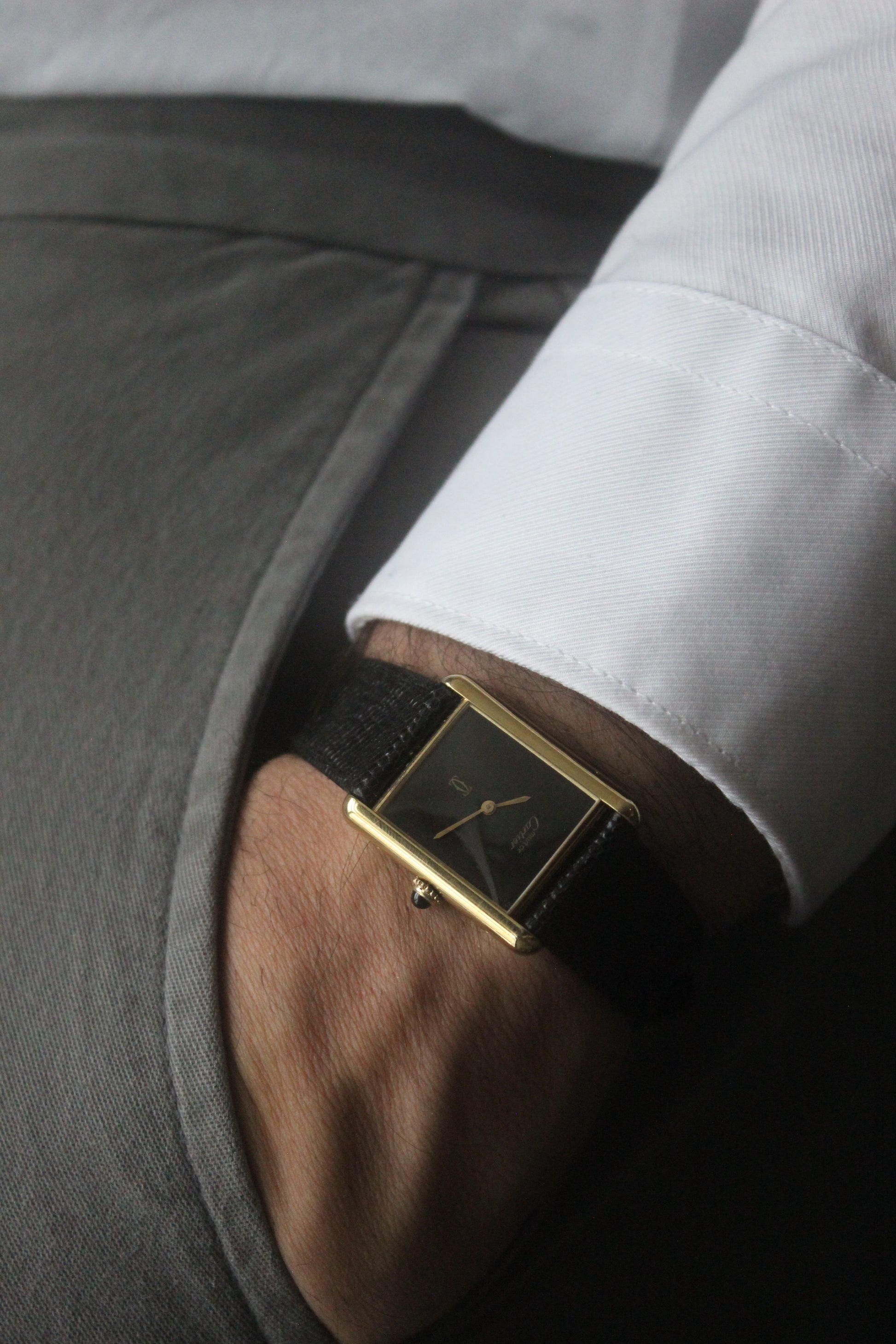 A Must de Cartier Tank watch with a yellow gold-plated sterling silver case, deep black ghost dial, and gold-tone hands. The watch is paired with a black lizard strap and features a cabochon crown. 