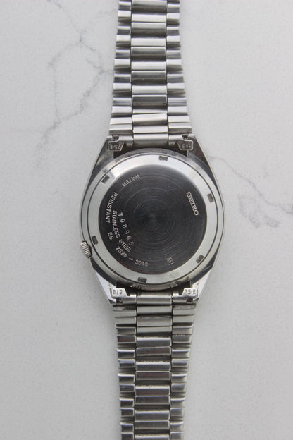 The case back of a vintage Seiko 5 automatic wristwatch (Reference Number: 7S26-3040) made of stainless steel. The screw-down case back is engraved with Seiko branding, water resistance details, and serial numbers, showing visible signs of wear including surface scratches. The original stainless steel bracelet is attached, featuring end links marked "B13" and "75-E". This Japan-exclusive mid-1980s model is in good condition with expected wear for its age.