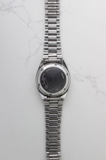 The case back of a vintage Seiko 5 automatic wristwatch (Reference Number: 7S26-3040) made of stainless steel. The screw-down case back is engraved with Seiko branding, water resistance details, and serial numbers, showing visible signs of wear including surface scratches. The original stainless steel bracelet is attached, featuring end links marked "B13" and "75-E". This Japan-exclusive mid-1980s model is in good condition with expected wear for its age.
