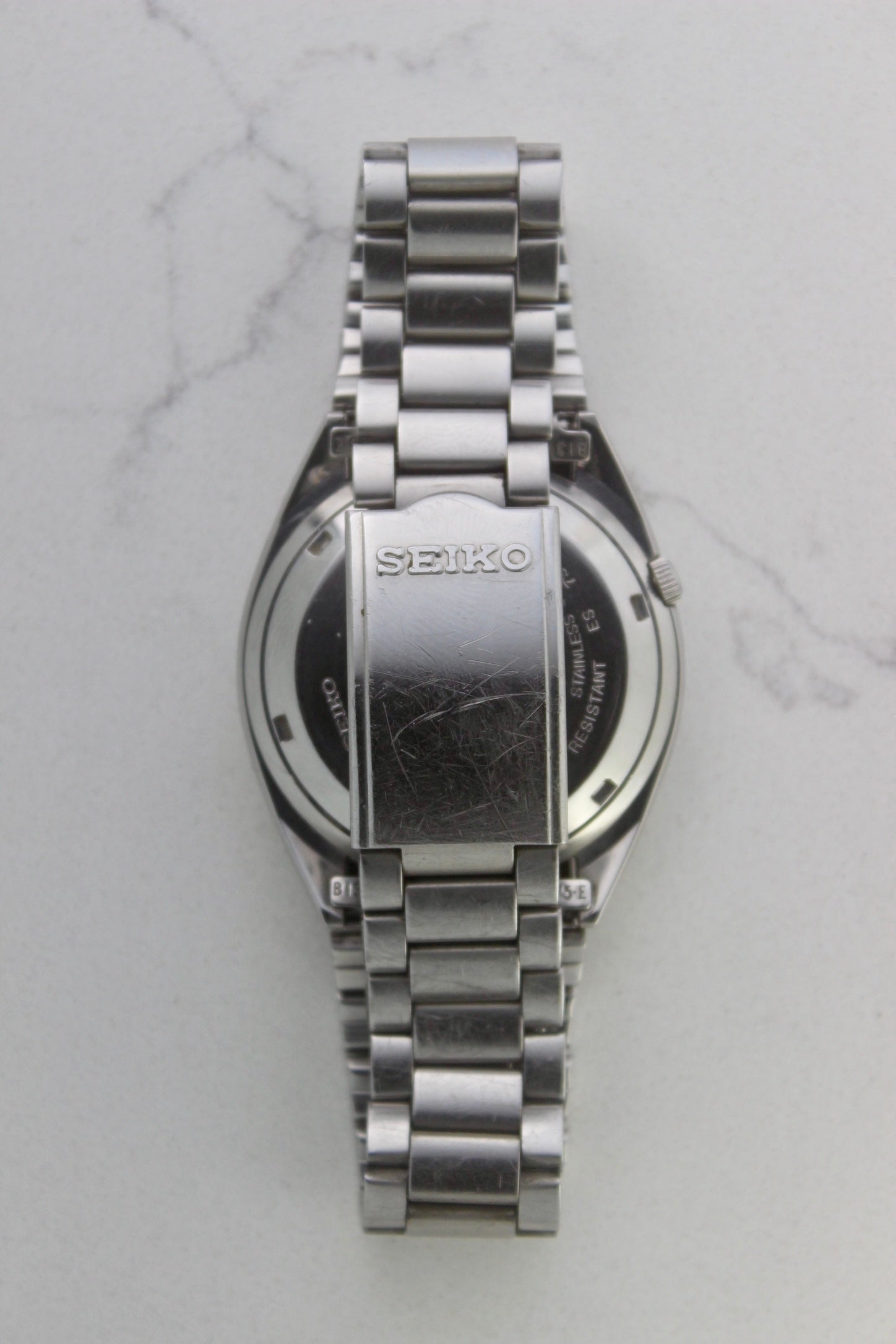 The stainless steel bracelet and clasp of a vintage Seiko 5 automatic wristwatch (Reference Number: 7S26-3040). The fold-over clasp is engraved with the Seiko logo and shows visible surface scratches, indicating signs of wear. The original stainless steel bracelet remains intact, with end links marked "B13" and "75-E". This Japan-exclusive mid-1980s model is in good condition with expected wear for its age.