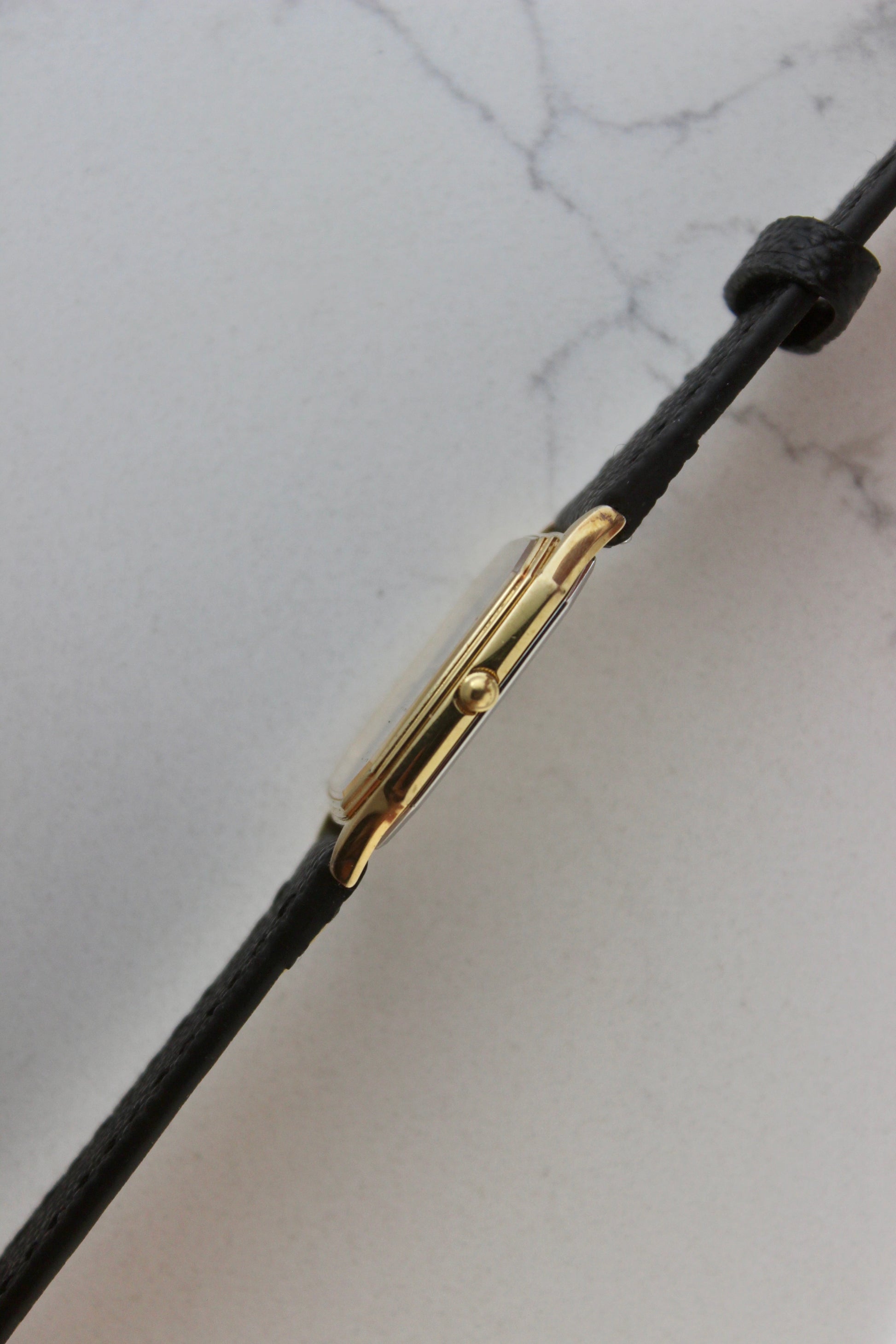A close-up of the Seiko Chariot 9021-5180
featuring a sleek rectangular gold-plated case, a black dial with minimalist gold indices, and delicate gold-tone hands. The modern yet timeless design is paired with a handmade black leather strap stitched with beige accents for a refined look.