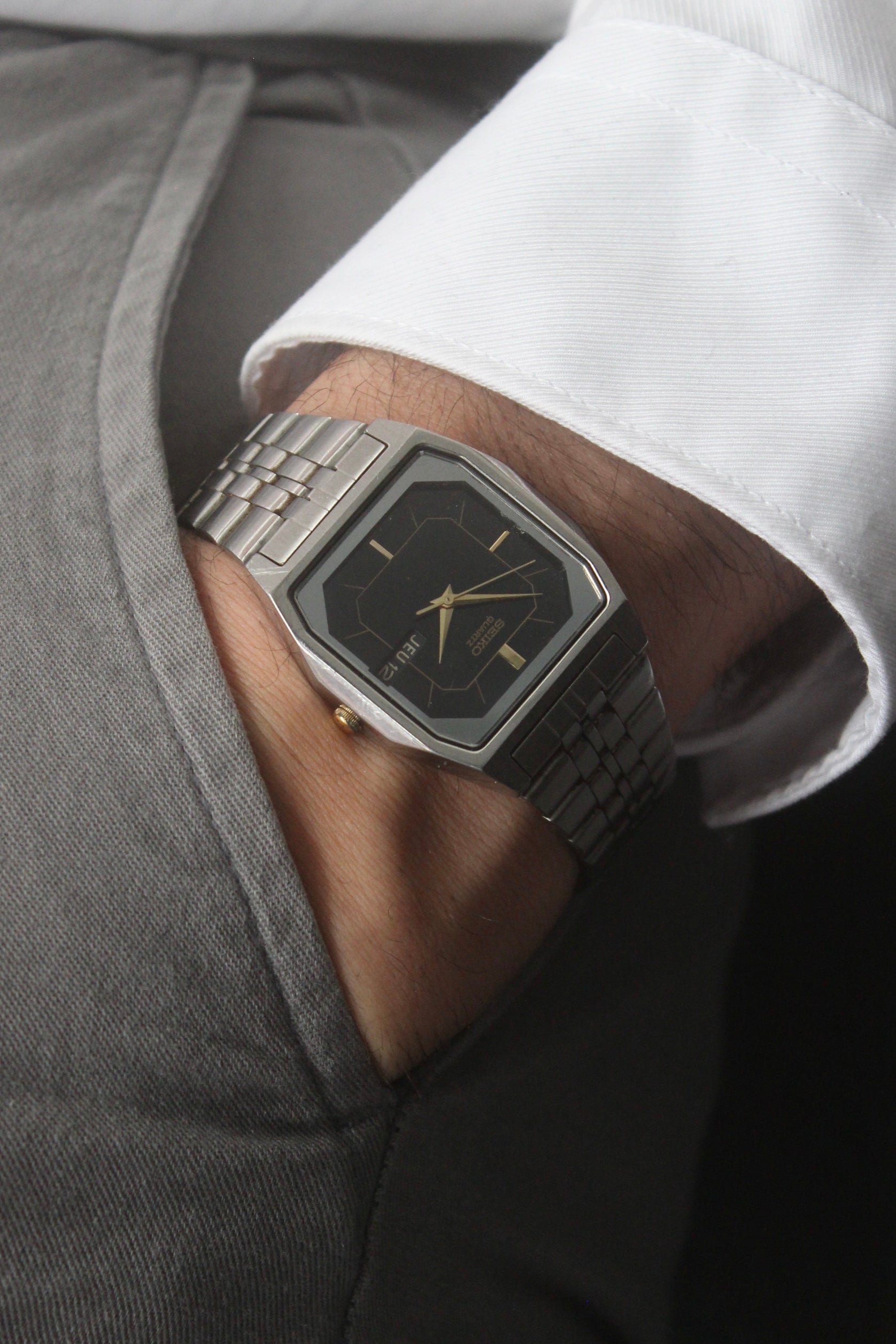 A close-up of the Seiko Dolce Quartz 7N43-5011, featuring a rectangular stainless steel case, black dial with gold accents, and a day-date window at 3 o'clock. The watch is paired with a stainless steel bracelet, exuding a timeless and versatile design.