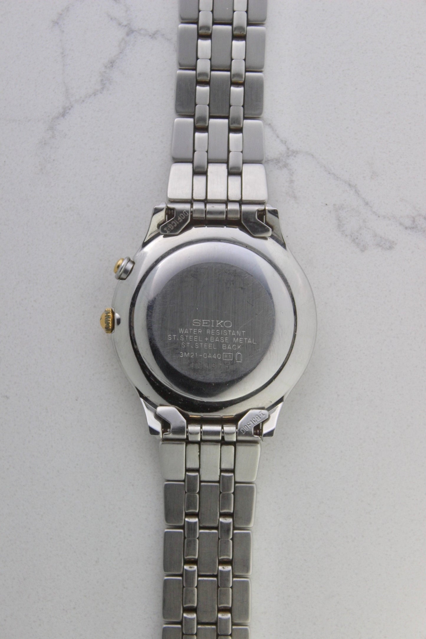 vintage Seiko Dolce AGS wristwatch with a two-tone stainless steel and gold-plated bracelet, set against a light-colored marble background. The watch features a pearl white sunburst dial with gold-plated stick indices and hands. The fixed bezel is stainless steel with gold accents. The case measures approximately 37mm in diameter and 41mm lug to lug. The dial includes the text
'Seiko AGS' at the top and 'Dolce' at the bottom. A gold-toned crown is positioned at 3 o'clock. 