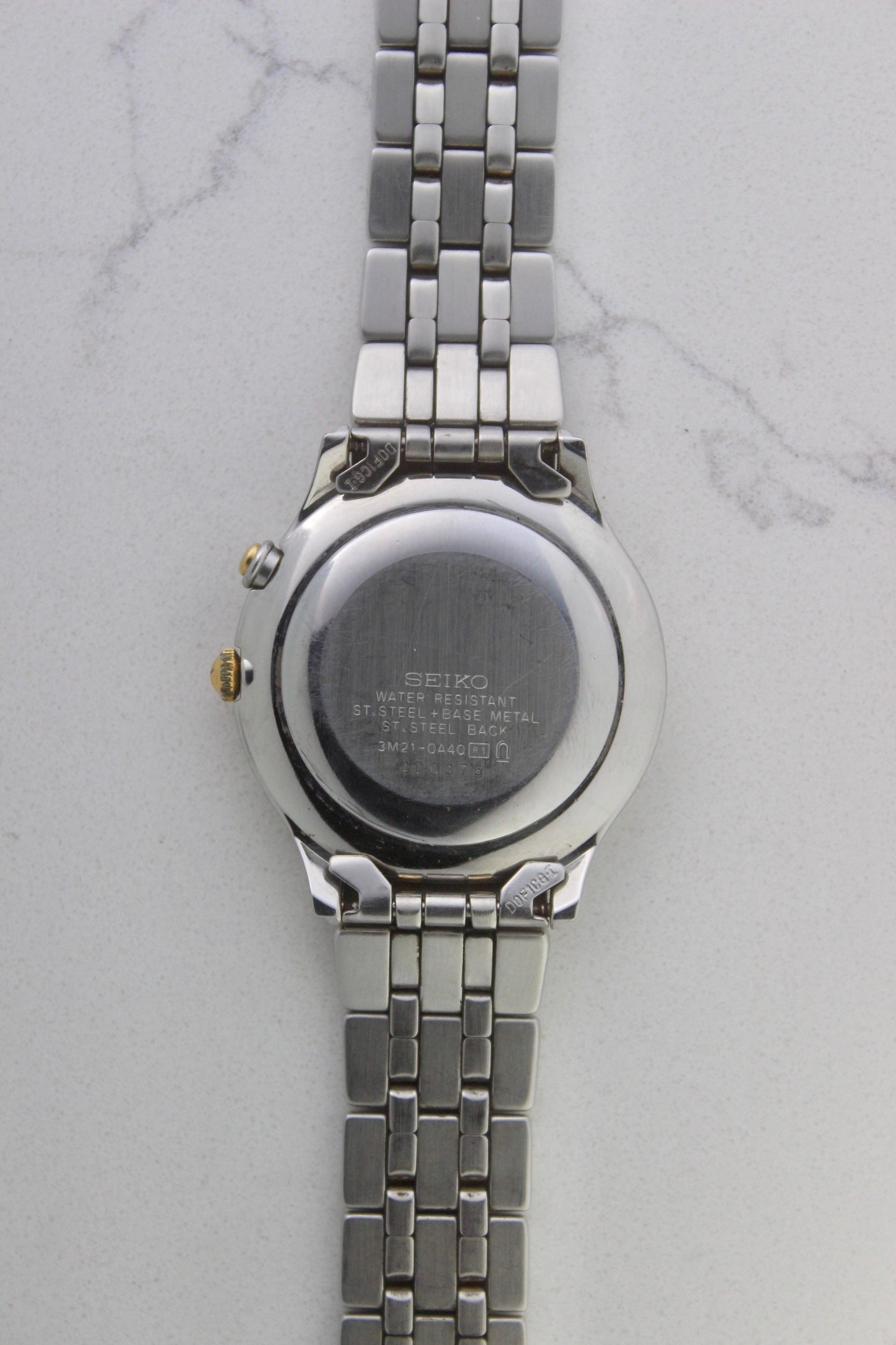 vintage Seiko Dolce AGS wristwatch with a two-tone stainless steel and gold-plated bracelet, set against a light-colored marble background. The watch features a pearl white sunburst dial with gold-plated stick indices and hands. The fixed bezel is stainless steel with gold accents. The case measures approximately 37mm in diameter and 41mm lug to lug. The dial includes the text
'Seiko AGS' at the top and 'Dolce' at the bottom. A gold-toned crown is positioned at 3 o'clock. 