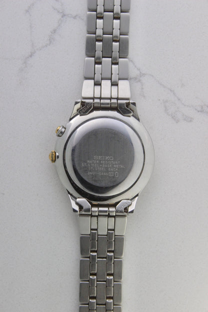 vintage Seiko Dolce AGS wristwatch with a two-tone stainless steel and gold-plated bracelet, set against a light-colored marble background. The watch features a pearl white sunburst dial with gold-plated stick indices and hands. The fixed bezel is stainless steel with gold accents. The case measures approximately 37mm in diameter and 41mm lug to lug. The dial includes the text
'Seiko AGS' at the top and 'Dolce' at the bottom. A gold-toned crown is positioned at 3 o'clock. 