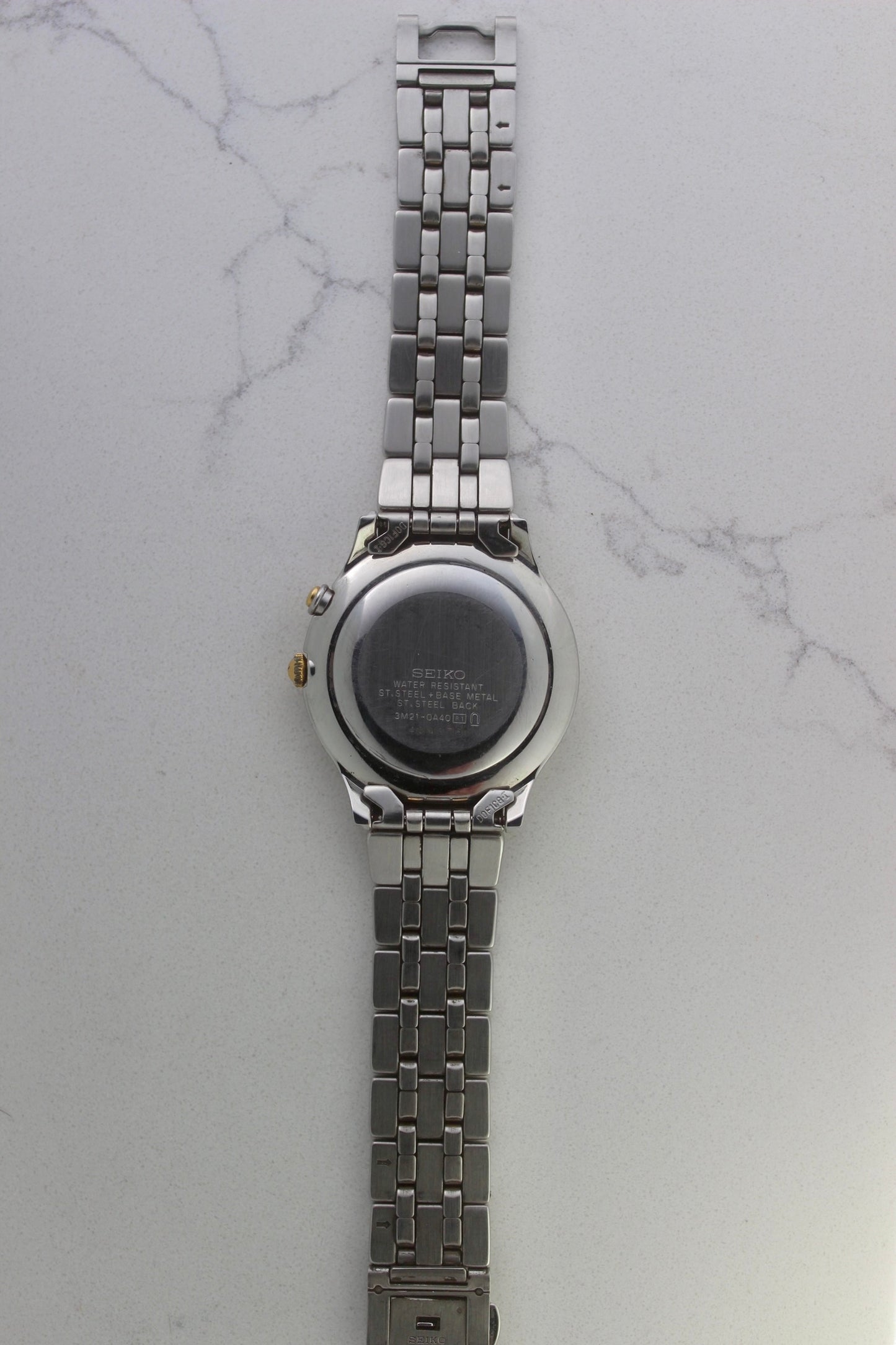 vintage Seiko Dolce AGS wristwatch with a two-tone stainless steel and gold-plated bracelet, set against a light-colored marble background. The watch features a pearl white sunburst dial with gold-plated stick indices and hands. The fixed bezel is stainless steel with gold accents. The case measures approximately 37mm in diameter and 41mm lug to lug. The dial includes the text
'Seiko AGS' at the top and 'Dolce' at the bottom. A gold-toned crown is positioned at 3 o'clock. 