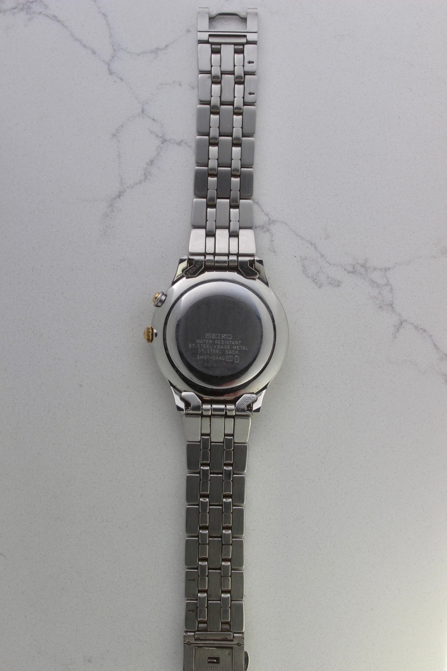 vintage Seiko Dolce AGS wristwatch with a two-tone stainless steel and gold-plated bracelet, set against a light-colored marble background. The watch features a pearl white sunburst dial with gold-plated stick indices and hands. The fixed bezel is stainless steel with gold accents. The case measures approximately 37mm in diameter and 41mm lug to lug. The dial includes the text
'Seiko AGS' at the top and 'Dolce' at the bottom. A gold-toned crown is positioned at 3 o'clock. 