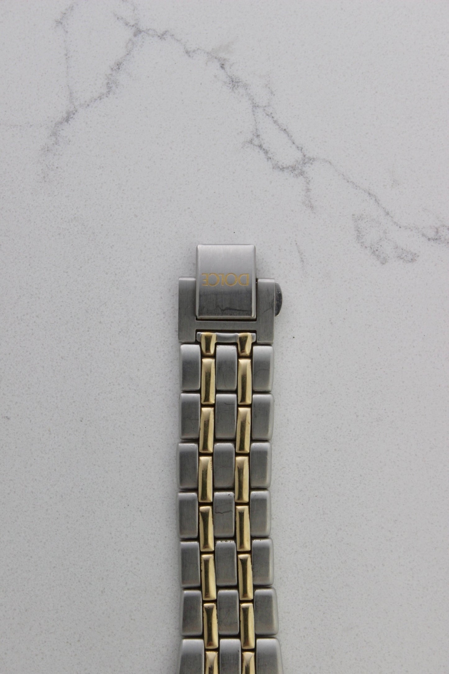 vintage Seiko Dolce AGS wristwatch with a two-tone stainless steel and gold-plated bracelet, set against a light-colored marble background. The watch features a pearl white sunburst dial with gold-plated stick indices and hands. The fixed bezel is stainless steel with gold accents. The case measures approximately 37mm in diameter and 41mm lug to lug. The dial includes the text
'Seiko AGS' at the top and 'Dolce' at the bottom. A gold-toned crown is positioned at 3 o'clock. 