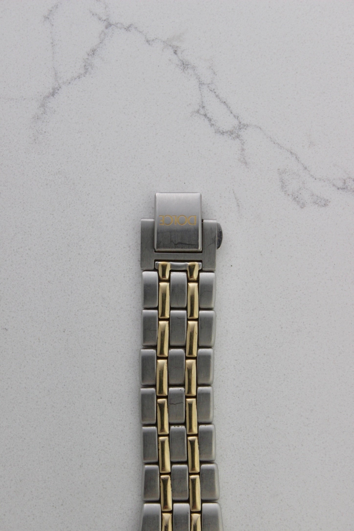vintage Seiko Dolce AGS wristwatch with a two-tone stainless steel and gold-plated bracelet, set against a light-colored marble background. The watch features a pearl white sunburst dial with gold-plated stick indices and hands. The fixed bezel is stainless steel with gold accents. The case measures approximately 37mm in diameter and 41mm lug to lug. The dial includes the text
'Seiko AGS' at the top and 'Dolce' at the bottom. A gold-toned crown is positioned at 3 o'clock. 