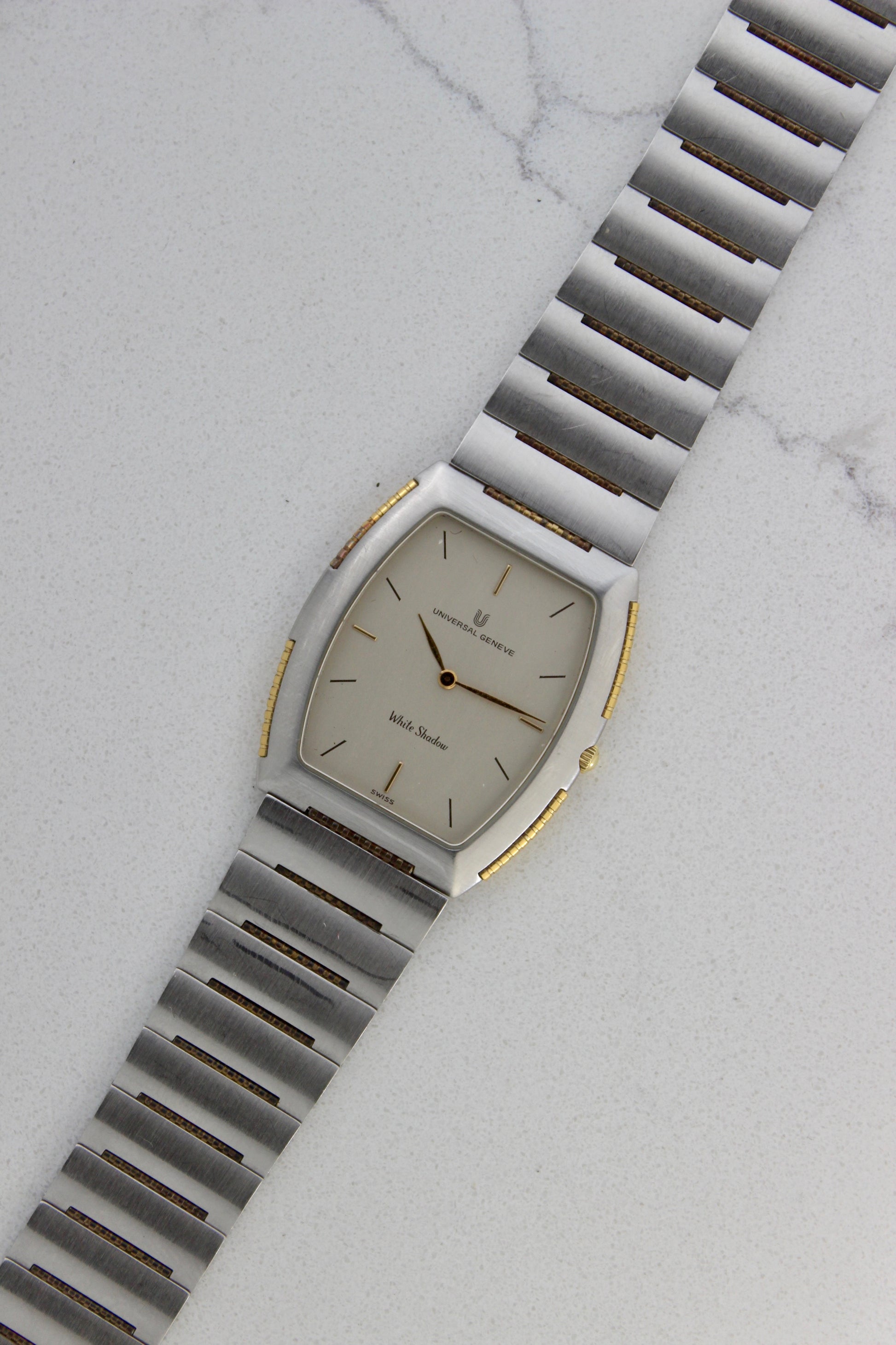 Front View of Universal Genève White Shadow Ref. 617-020
A close-up of the Universal Genève White Shadow Ref. 617-020, featuring a sleek tonneau-shaped stainless steel case with gold accents, a clean white dial, and minimalist stick hands and indices. Paired with an integrated stainless steel bracelet for timeless elegance.