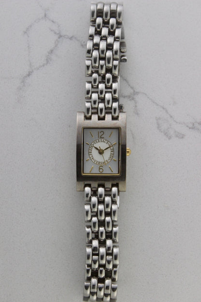 a rectangular stainless steel wristwatch with a silver-tone case and bracelet featuring a multi-link design. The watch face has a while dial with gold-tone hour makers, hands, and a cirular logo pattern that reads 'ALFREDO VERSACE'. The crown is gold-tone and positioned on the right side of the case. The watch is displayed against a light marble surface background. 