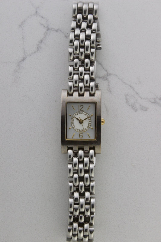 a rectangular stainless steel wristwatch with a silver-tone case and bracelet featuring a multi-link design. The watch face has a while dial with gold-tone hour makers, hands, and a cirular logo pattern that reads 'ALFREDO VERSACE'. The crown is gold-tone and positioned on the right side of the case. The watch is displayed against a light marble surface background. 