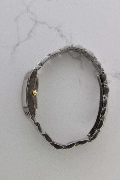 a rectangular stainless steel wristwatch with a silver-tone case and bracelet featuring a multi-link design. The watch face has a while dial with gold-tone hour makers, hands, and a cirular logo pattern that reads 'ALFREDO VERSACE'. The crown is gold-tone and positioned on the right side of the case. The watch is displayed against a light marble surface background. 