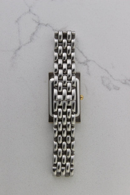 a rectangular stainless steel wristwatch with a silver-tone case and bracelet featuring a multi-link design. The watch face has a while dial with gold-tone hour makers, hands, and a cirular logo pattern that reads 'ALFREDO VERSACE'. The crown is gold-tone and positioned on the right side of the case. The watch is displayed against a light marble surface background. 